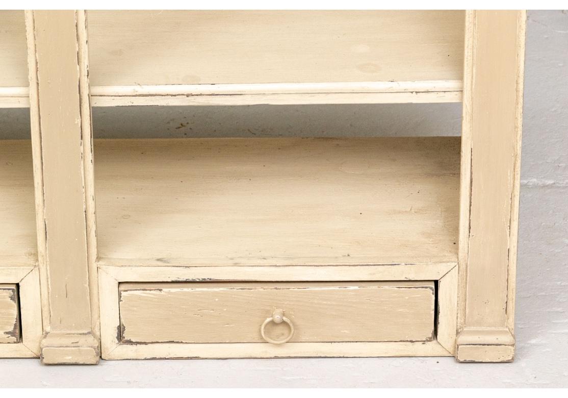 An interesting design with three adjustable shelves and three lower drawers. The openwork front frame with three arches. and pilaster supports. Painted overall in a cream-taupe tone. 
H. 58 1/2