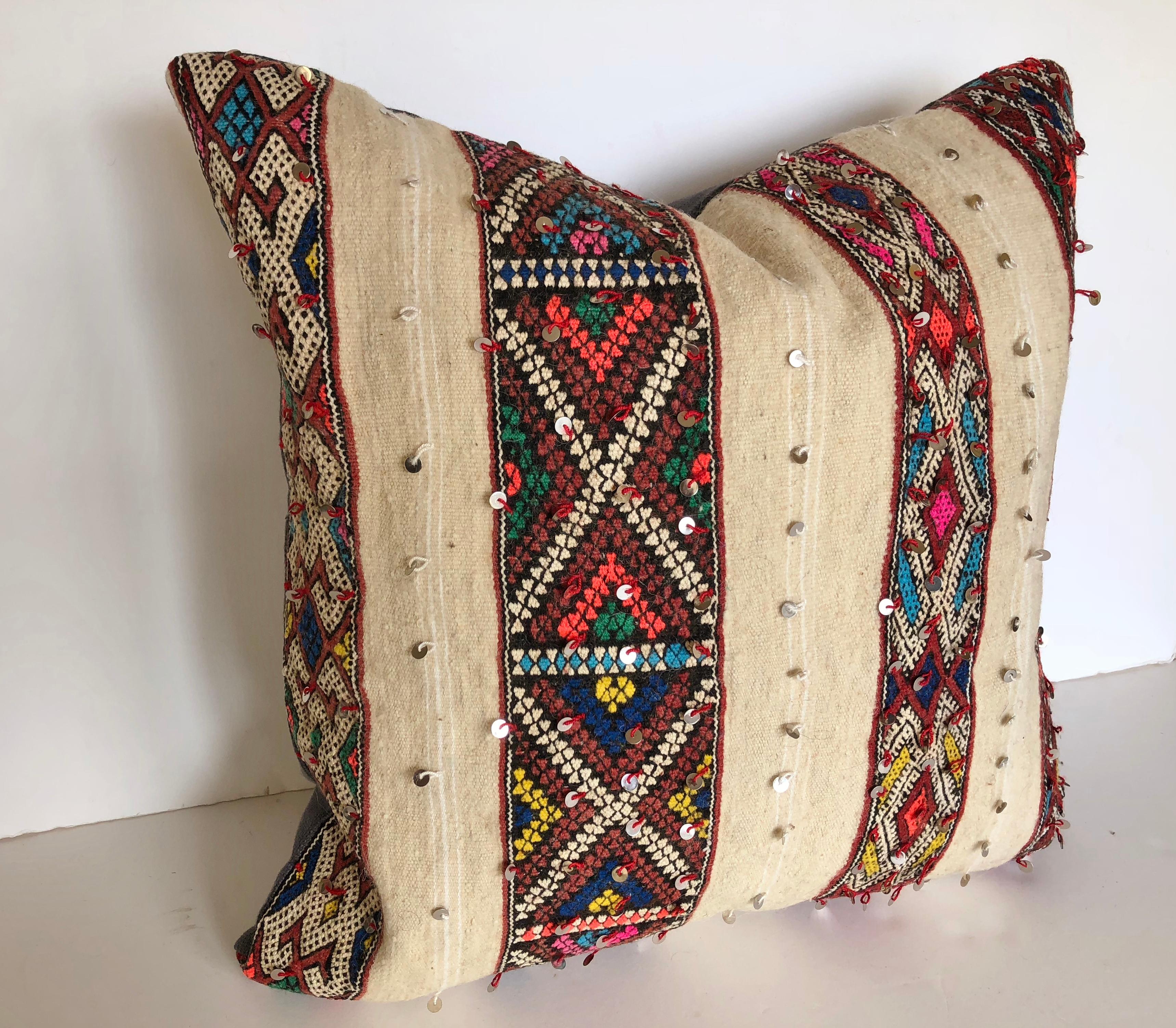 Custom pillow cut from a vintage hand loomed wool vintage Moroccan rug made by the Berber women of the Atlas Mountains. Brightly colored bands are embellished with sequins against a creamy wool textile. Pillow is backed in purple linen, filled with