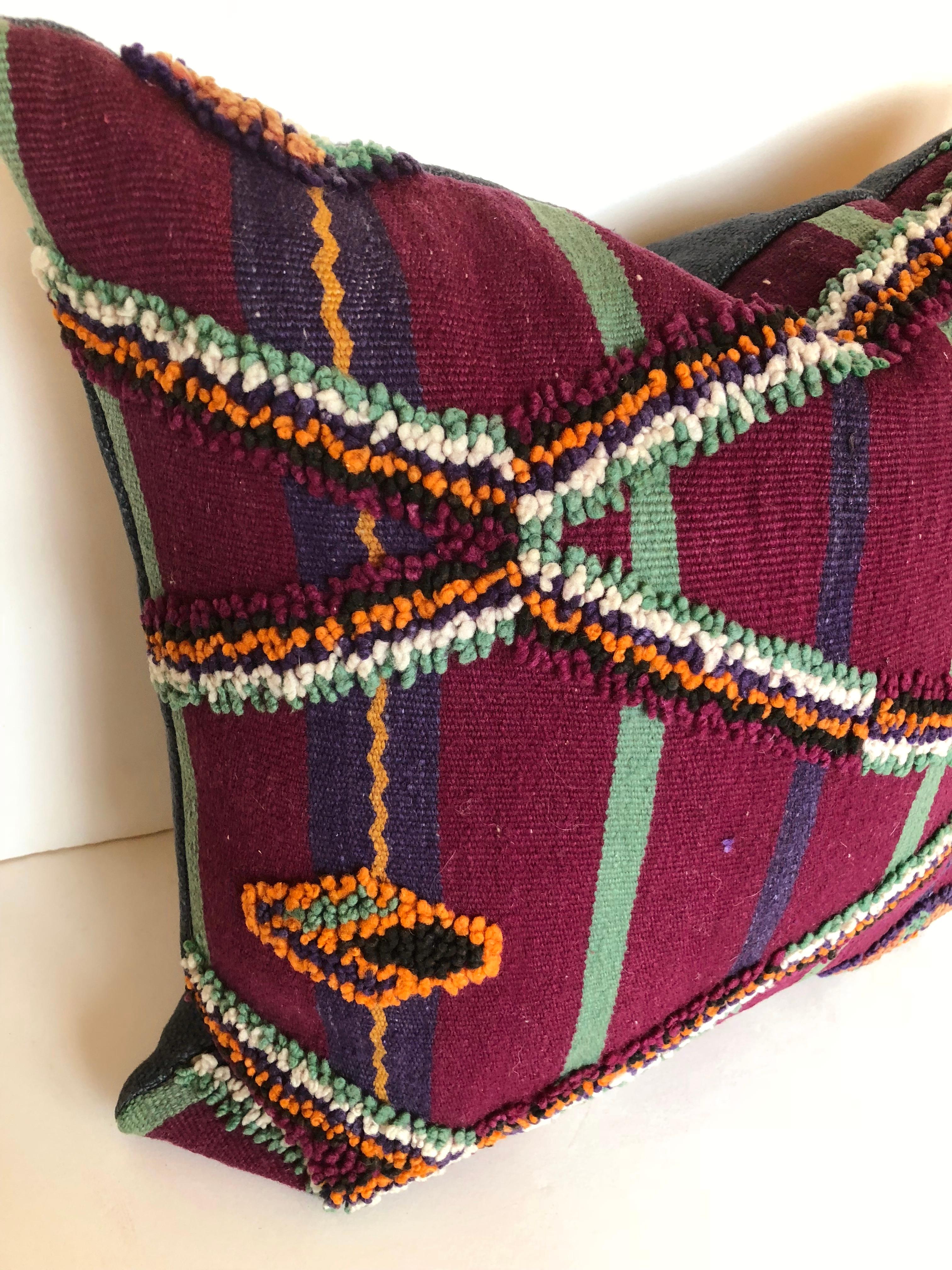 Custom pillow cut from a vintage hand-loomed Moroccan wool Berber rug from the Atlas Mountains. Woven wool stripes are embellished with tufted tribal designs. Pillow is backed in deep blue linen, filled with an insert of 50/50 down and feathers and