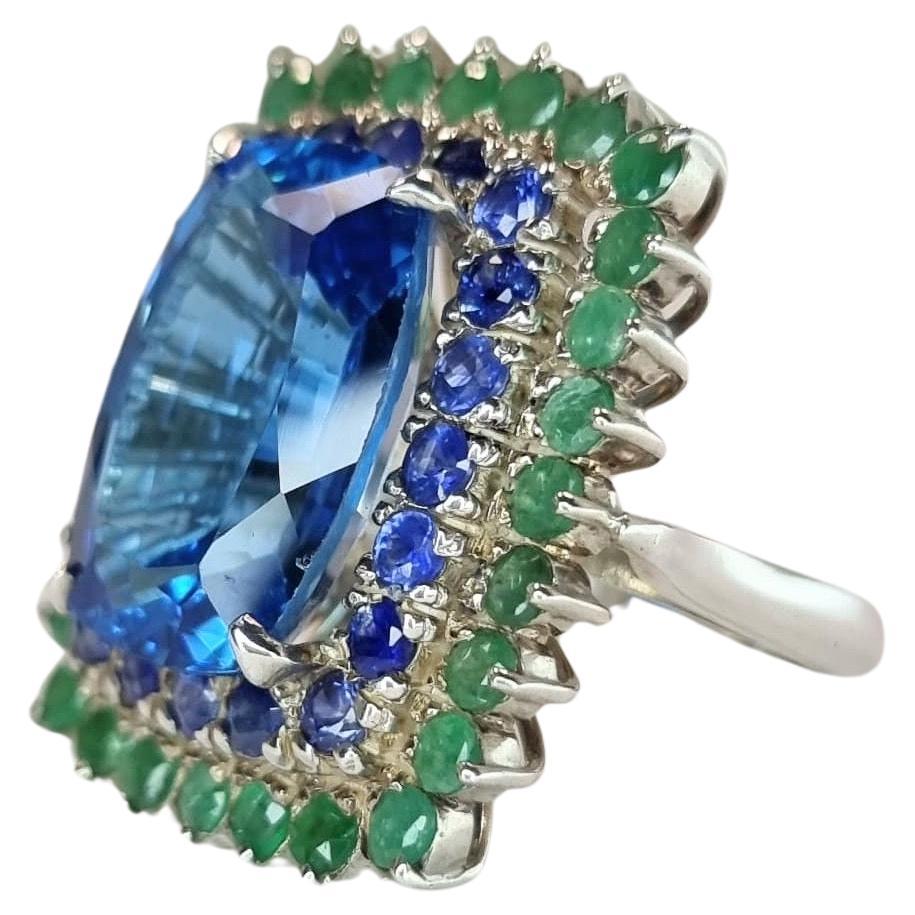 Anillo de cóctel personalizado de topacio azul en platino con halo de esmeralda y zafiro