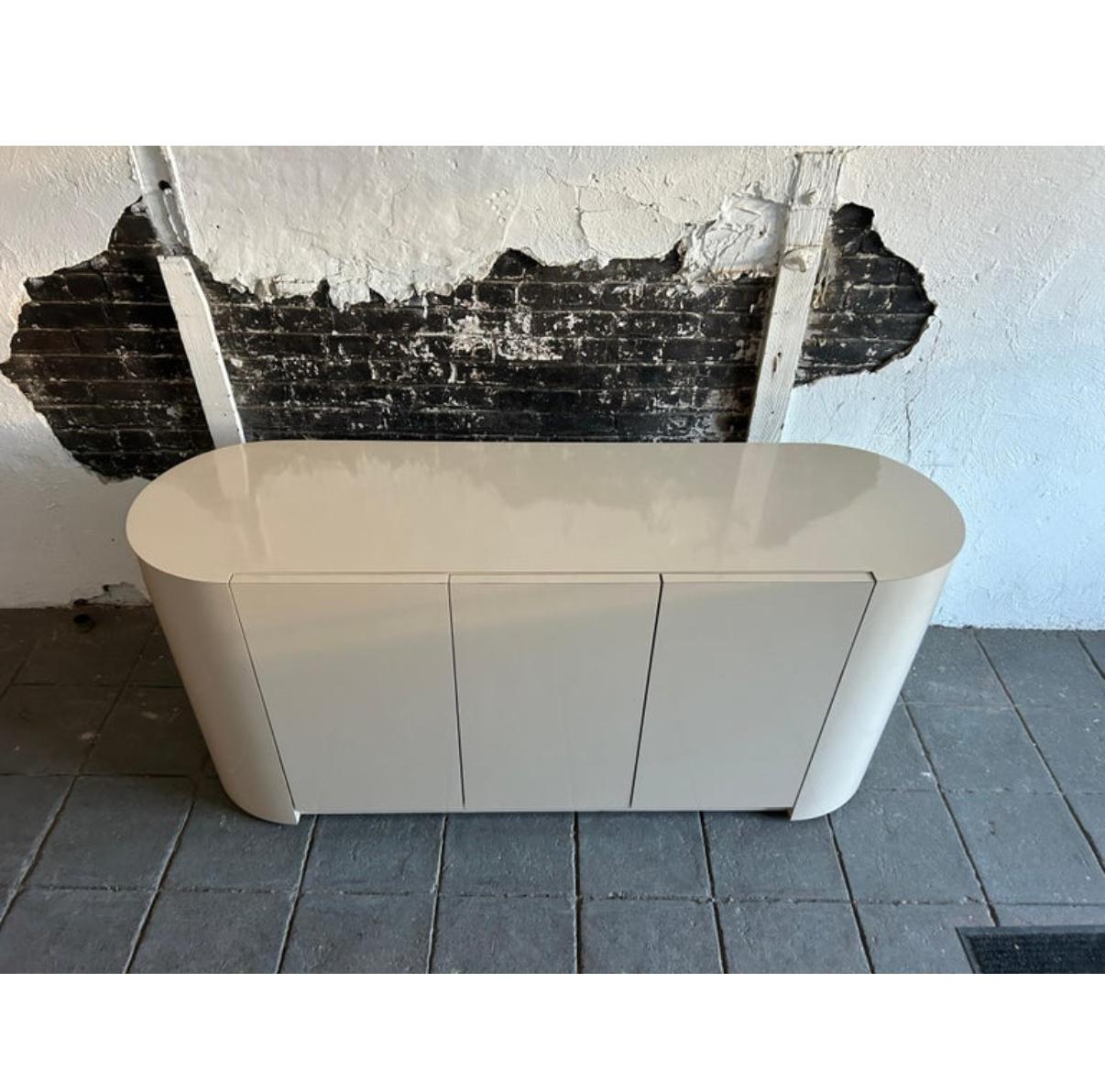 Aparador postmoderno pop art de 3 puertas de color beige con forma de pastilla y extremos redondeados. El aparador de laminado brillante de color beige muy claro fabricado a medida hacia 1980 tiene 3 puertas de armario con cierres. Detrás de las