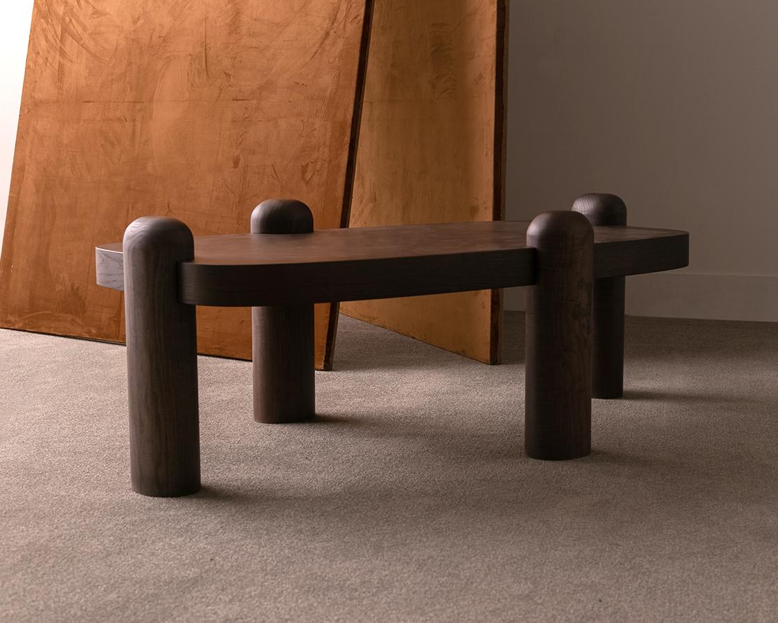 Eine sieben Zentimeter hohe Tischplatte wird von ovalisierten Holzsäulen getragen. Diese Kombination aus Couchtisch und Beistelltisch zeichnet sich durch Stärke und Ausgewogenheit aus.  
Die aus Eichenfurnier und Massivholz gefertigten Tische bieten