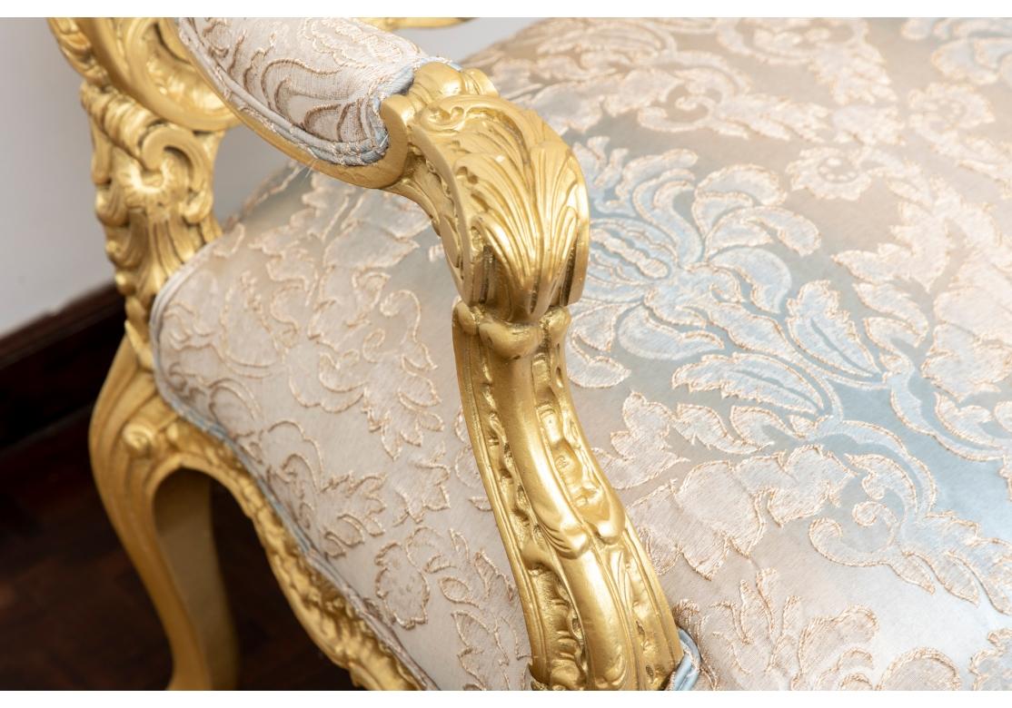 A very theatrical large throne chair in a custom treatment. With an intricately carved frame having stylized shells and scrolls with the foot a raised snail’s head motif and the entire frame in a dazzling gold paint. The custom fabric a silk-like