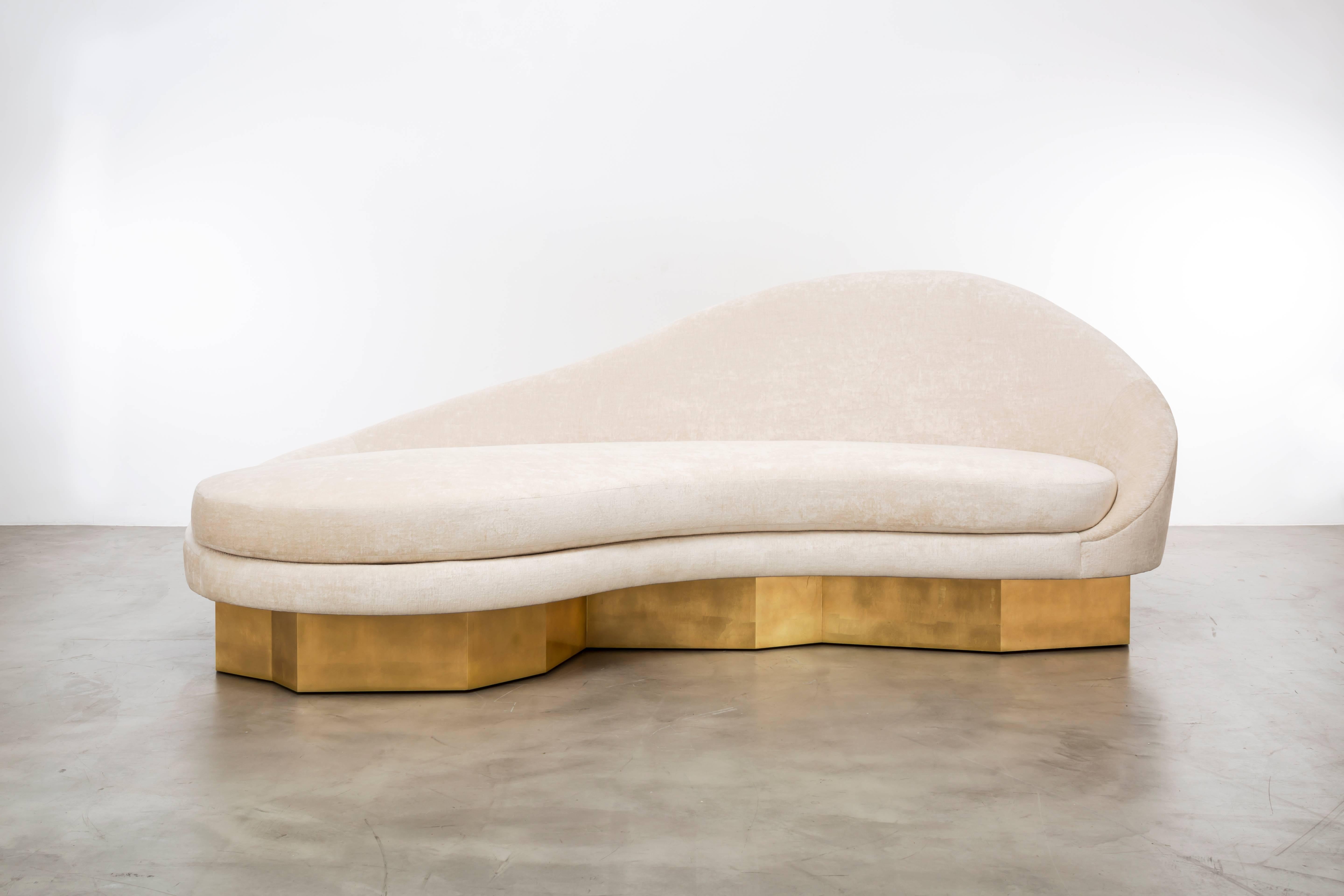 The Satine sofa, inspired by the curvature of Gaudi architecture, features an asymmetrical sophisticated slope that meets a fractured gold leaf plinth base to make a minimal and elegant statement. COM in a custom size of 96