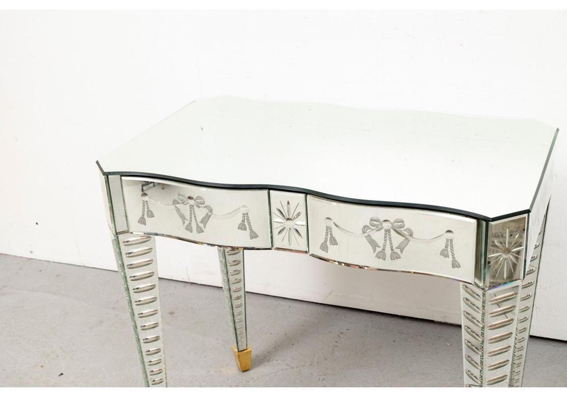 Superb serpentine form vanity with etched decoration under the mirrored surfaces. The frieze with two short drawers with etched ribbon garlands with bows and tassels, flanking a center star motif. Each with interior compartments. The sides and back