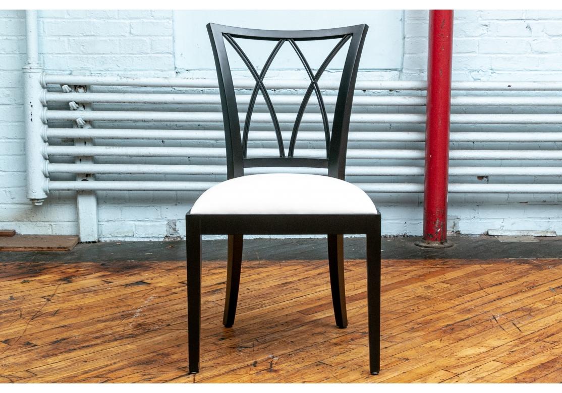 Two arm and six side chairs in a midcentury style with curved and open X form backs. The frames were custom ebonized, raised on square tapering legs, splayed in the back. The seats upholstered in off-white faux leather. 

Measures: height 37