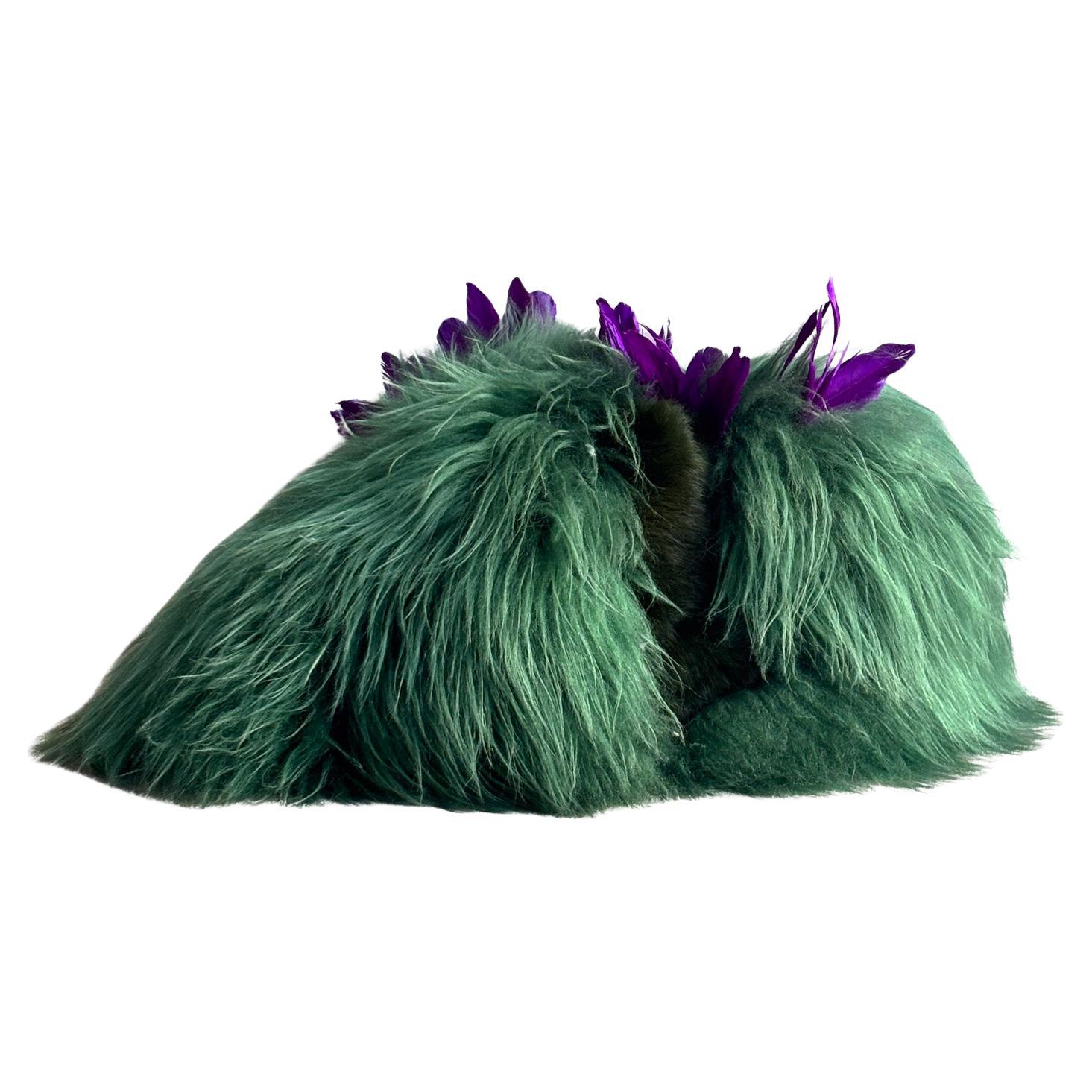 Ce pouf unique en peau de mouton verte avec des plumes violettes, créé par l'artiste belge Carine Boxy, incarne son approche de l'artisanat et des matériaux naturels. Fabriquée à la main à partir de peau de mouton teintée naturellement, chaque pièce