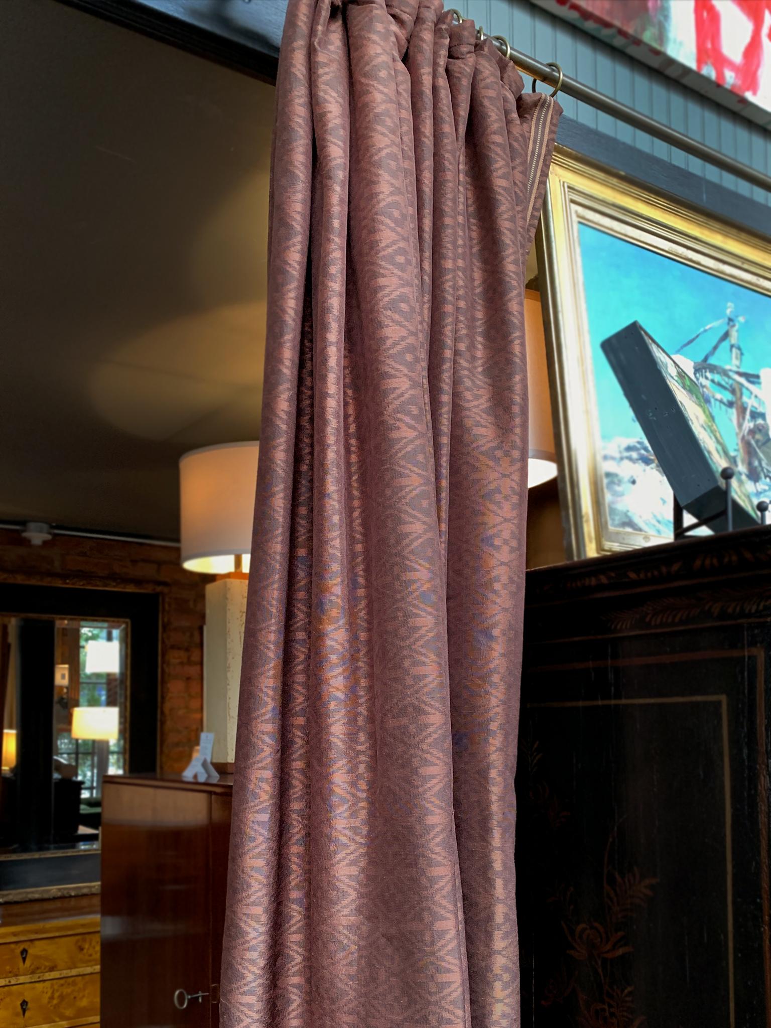 A set of 4 pleated silk curtain panels designed by Michael Smith and J.C. Landa. The fabric is a burgundy-bronze with a pearlescent sheen. Diamond motifs decorate the silk in an elegant ikat pattern, while a multi-toned trim runs along the sides of