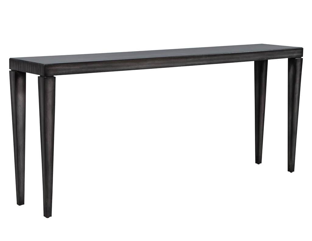 This elegant console table is part of the Carrocel custom collection. It is finished in a hand-rubbed and polished grey stain, with tapered legs and a rectangular top. A sleek and modern piece, perfect for any stylish home.