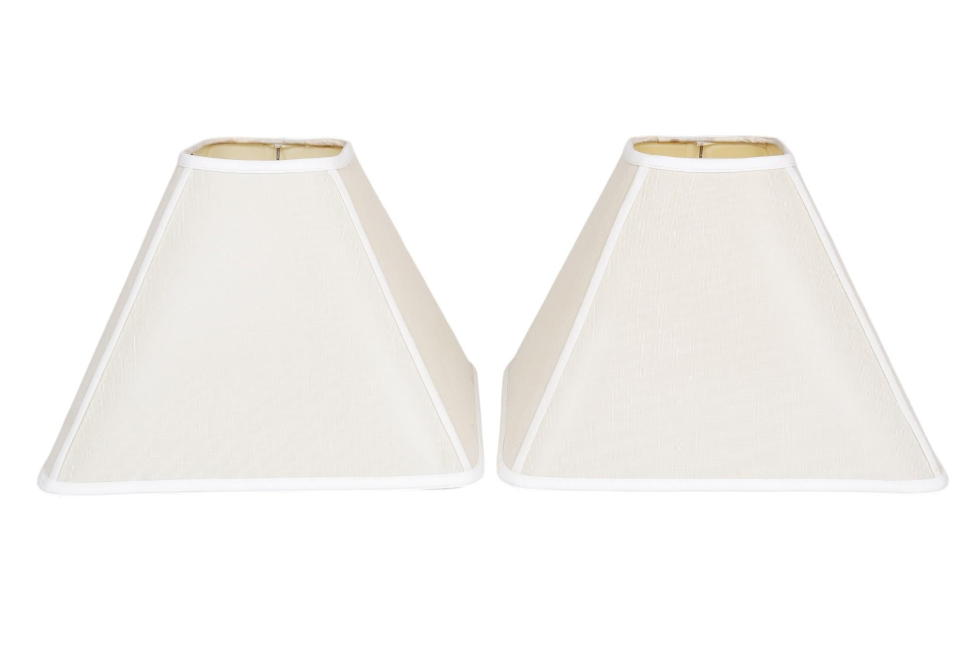 A pair of custom-made lamp shades. Square empire shaped lamp shades in natural linen are finished with a white trim. Dimensions per lamp shade. 