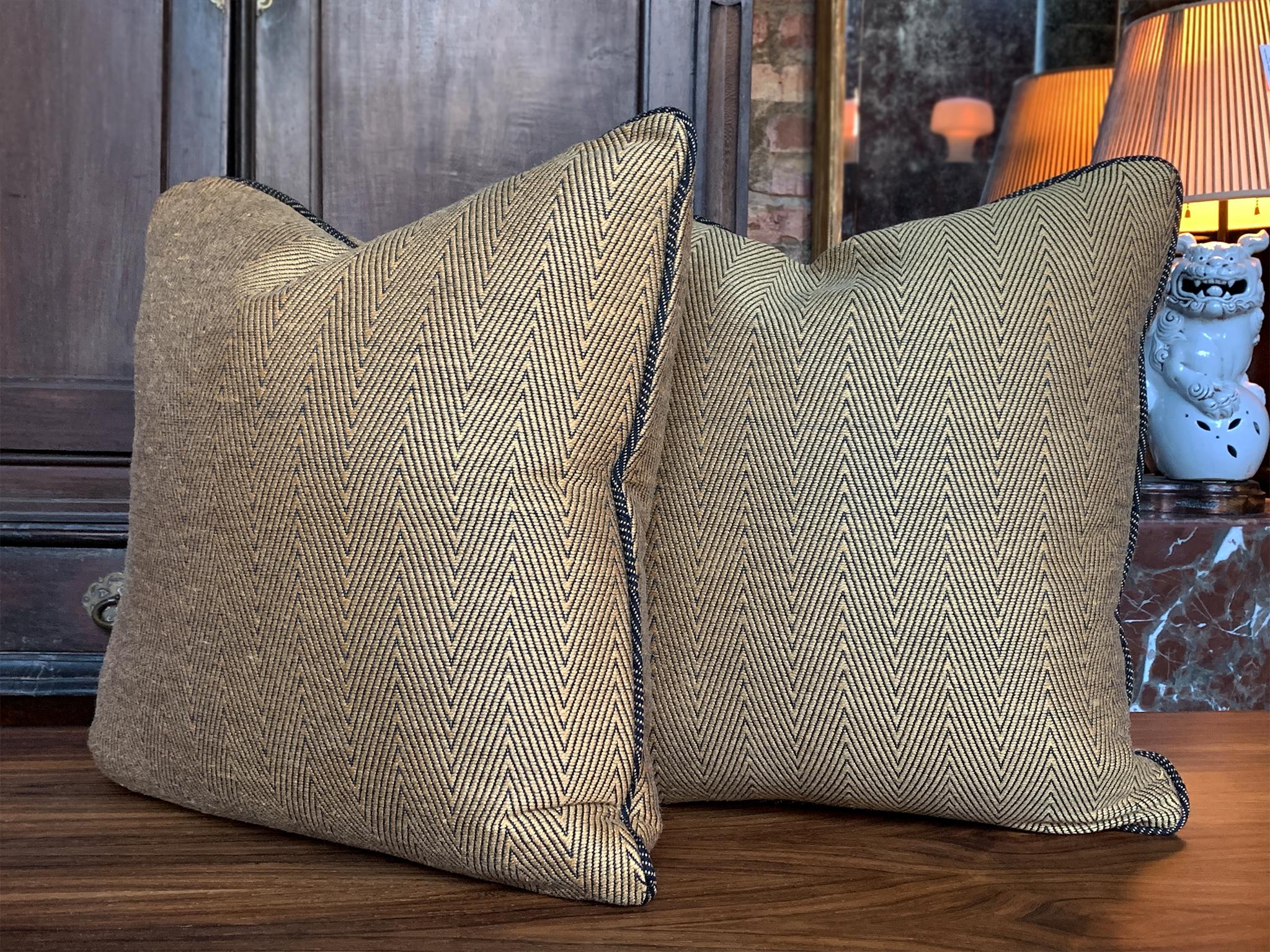 Un par de almohadas cuadradas personalizadas recién hechas en exclusiva para Cafiero Select. La funda es un exquisito tejido chevron de lana de Donghia. Es de un deslumbrante dorado y negro, con ribetes acordonados en un tono negro de contraste que