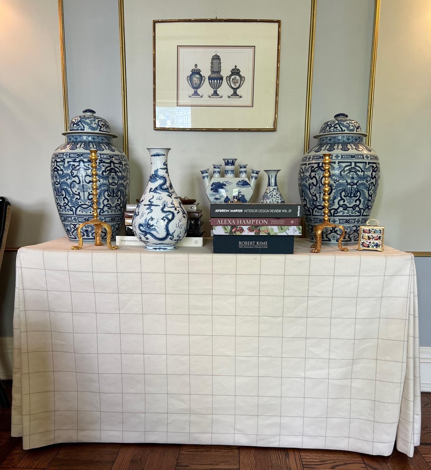 A tailored and timeless custom draped table, featuring a rectangular wood base enveloped in an elegant cream-toned fabric with a subtle tonal checkered grid. The fabric is precisely pleated at the corners for a structured, tailored effect, and