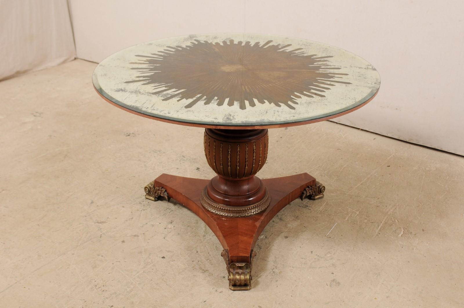 This fabulous custom center table has been fashioned with an artisan-made, round-shaped mirror top, with verre églomisé sunburst center, top which rests upon a vintage carved-wood pedestal base. The gold verre églomisé star or sunburst fills up the