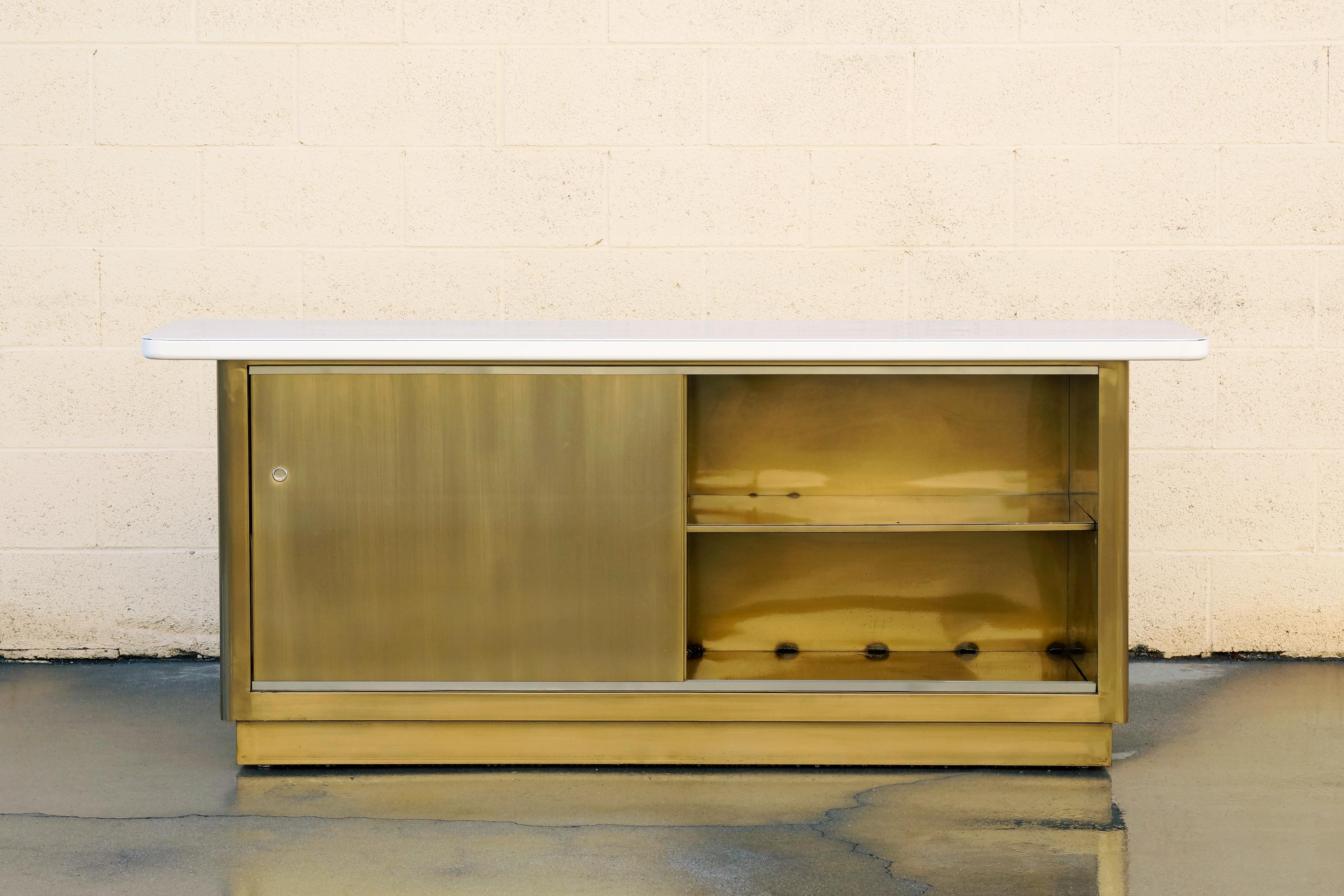 Custom made steel credenza inspired by tanker style furniture popular in the 1960s. This beauty features a two-tone brass and gloss white powder coated finish and double sliding doors with a single fixed shelf. Pairs perfectly with our custom