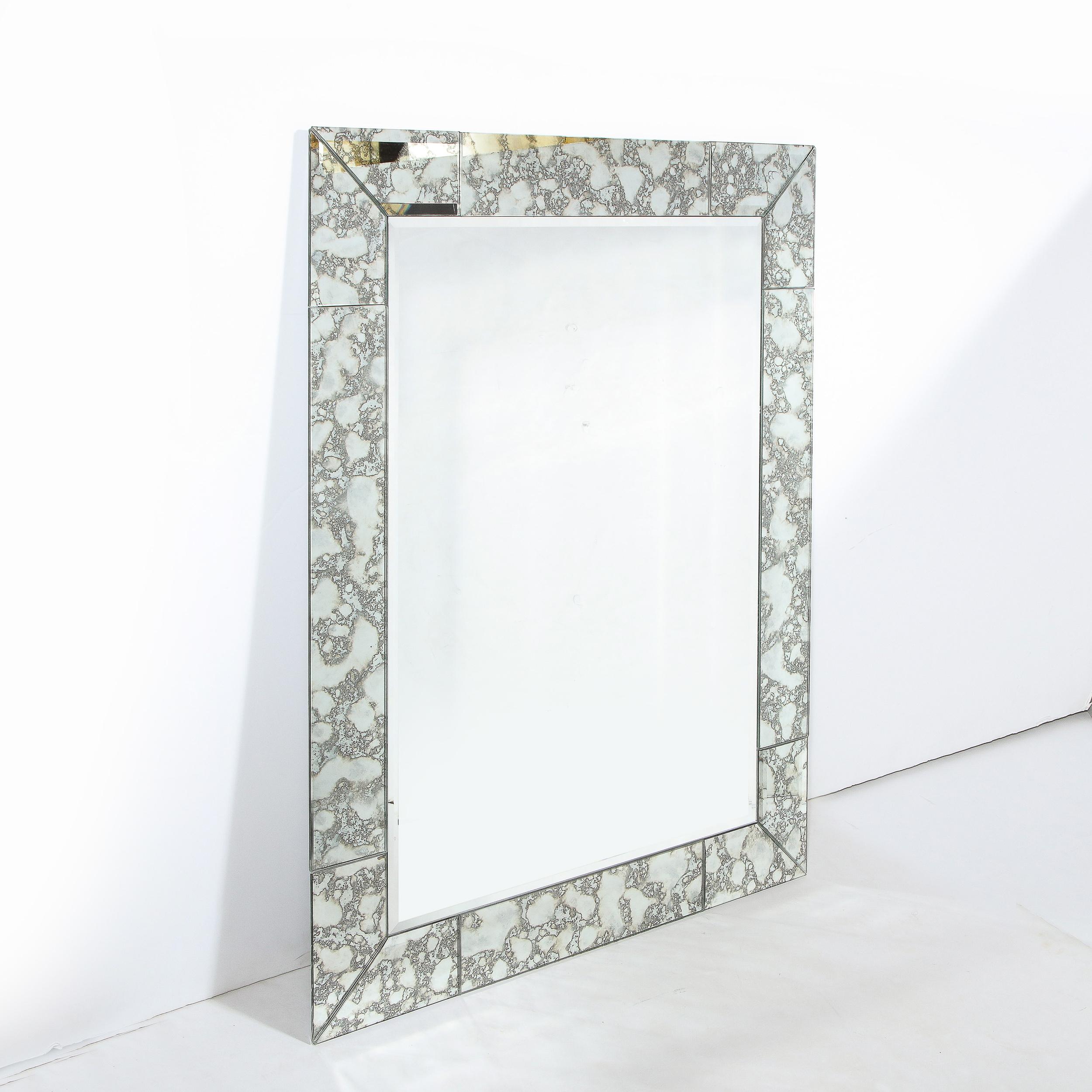 This stunning modern and customizable mirror was realized in the United States. It features a rectangular form with a tessellated border composed of rectilinear mirrored segments with beveled edges that wrap around the perimeter of the piece. The