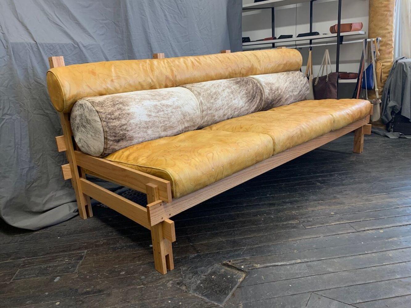 In the style of Sergio Rodrigues, this custom leather sofa was produced in 2021 by Brit Kleinman of AVO in Brooklyn. The solid oak frame holds upholstered, hand-tinted, marigold-yellow leather cushions and cowhide back cushions. 

Two