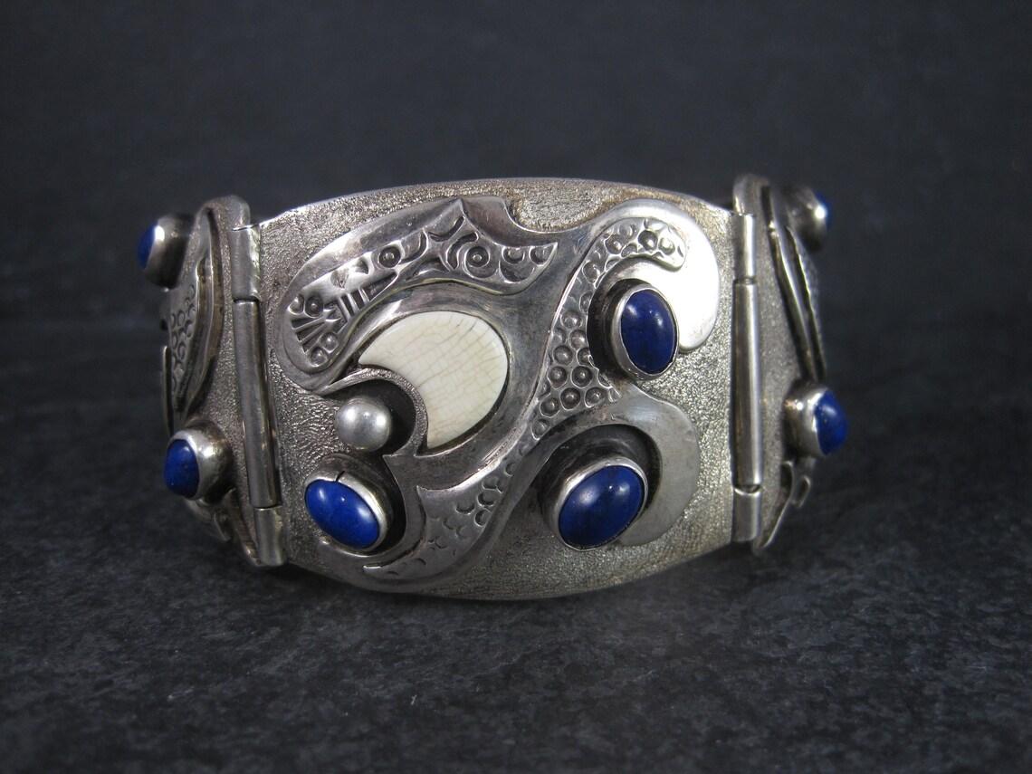 This gorgeous vintage sterling bracelet is a custom creation from the talented Teresa Archibeque.
It features 7 oval lapis lazuli gemstones and 3 fossilized ivory inlays.

This bracelet measures 1 7/16 inches wide and has a folding buckle type