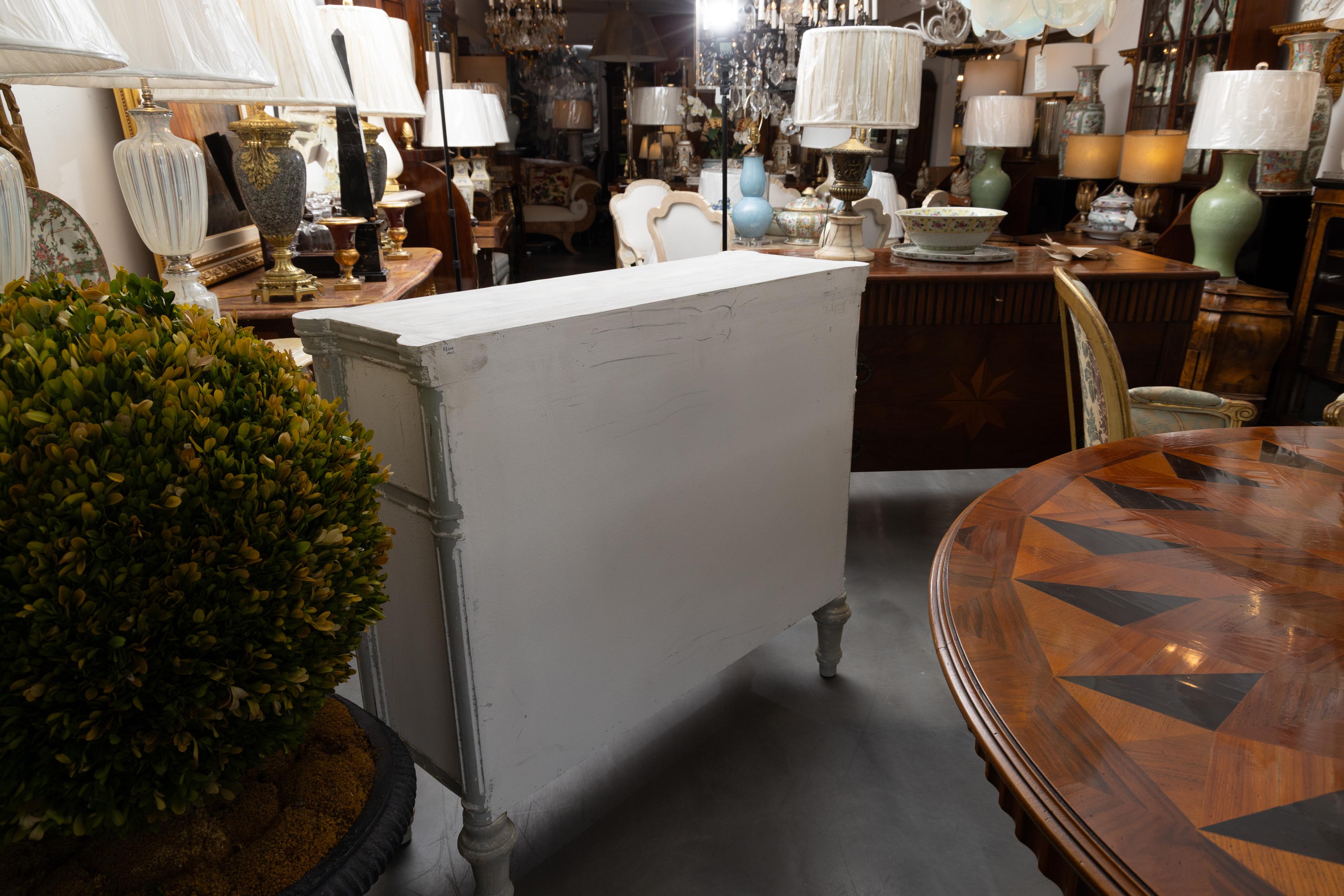 This is one of a pair of charming gray and white-washed chest of drawers.  The top with rounded corners is over three long drawers, the faces are decorated with parcel gilt cross hatches.