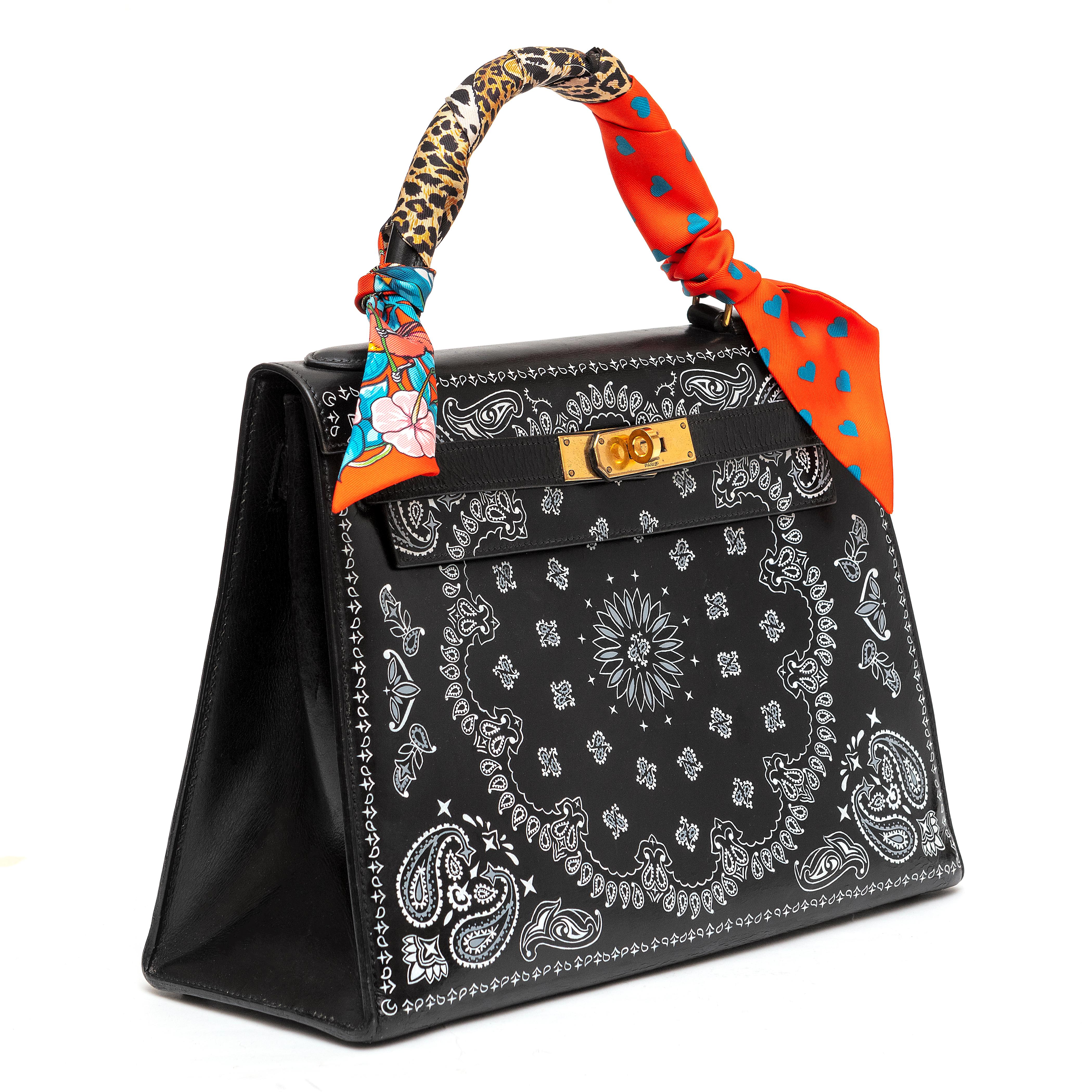 This one of a kind Hermès Kelly 28 in Box Leather features a white intricate bandana print and a Twilly. The bag is customized and the stencil is not original to the piece. Its black leather facade is offset with gold-tone hardware, and the