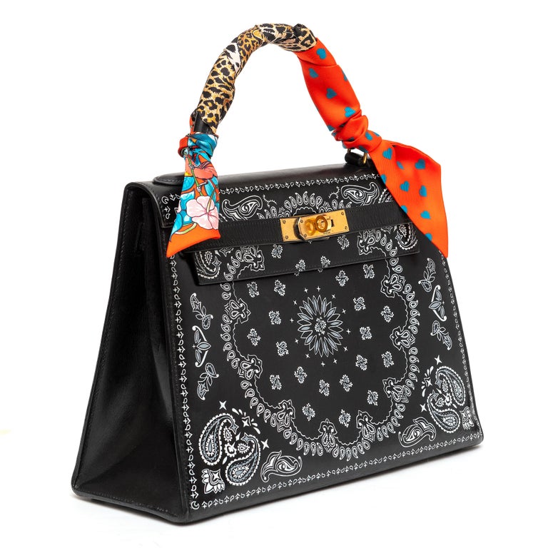 This one of a kind Hermès Kelly 28 in Box Leather features a white intricate bandana print and a Twilly. The bag is customized and the stencil is not original to the piece. Its black leather facade is offset with gold-tone hardware, and the
