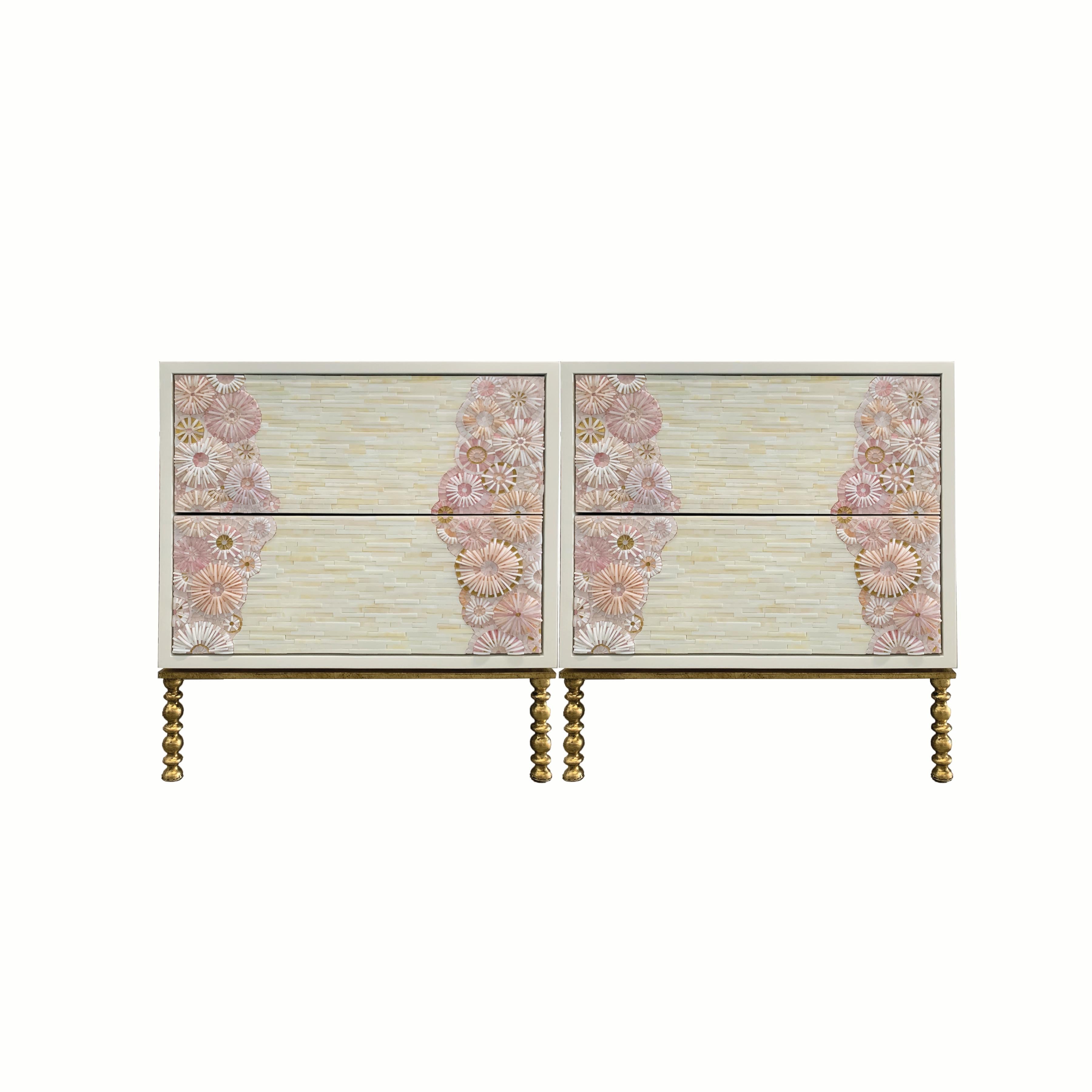 The blossom nightstand by Ercole Home has a 2-drawer front, with a white lacquer wood finish.
Handcut glass mosaic in variety shades of gold, pink, white and ivory decorate the surface in Blossom and stripe mosaic pattern.
The decorative metal