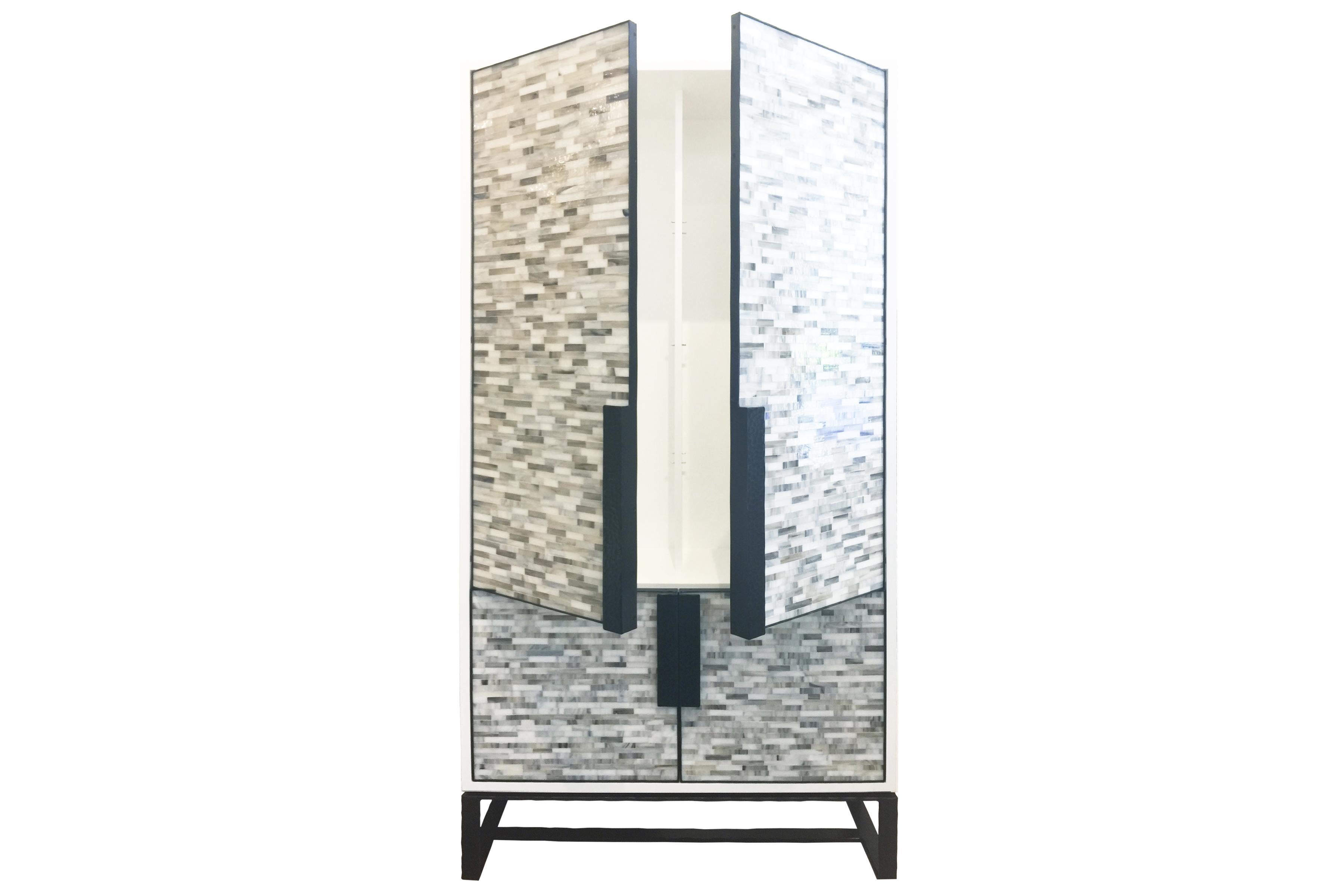 The Chelsea bar cabinet by Ercole Home has a 4-door front, with white lacquer wood finish on oak.
Hand cut glass mosaics in London grey and icy white decorate the surface in Luis pattern.
Hand-hammered metal framed doors, handles, and base in