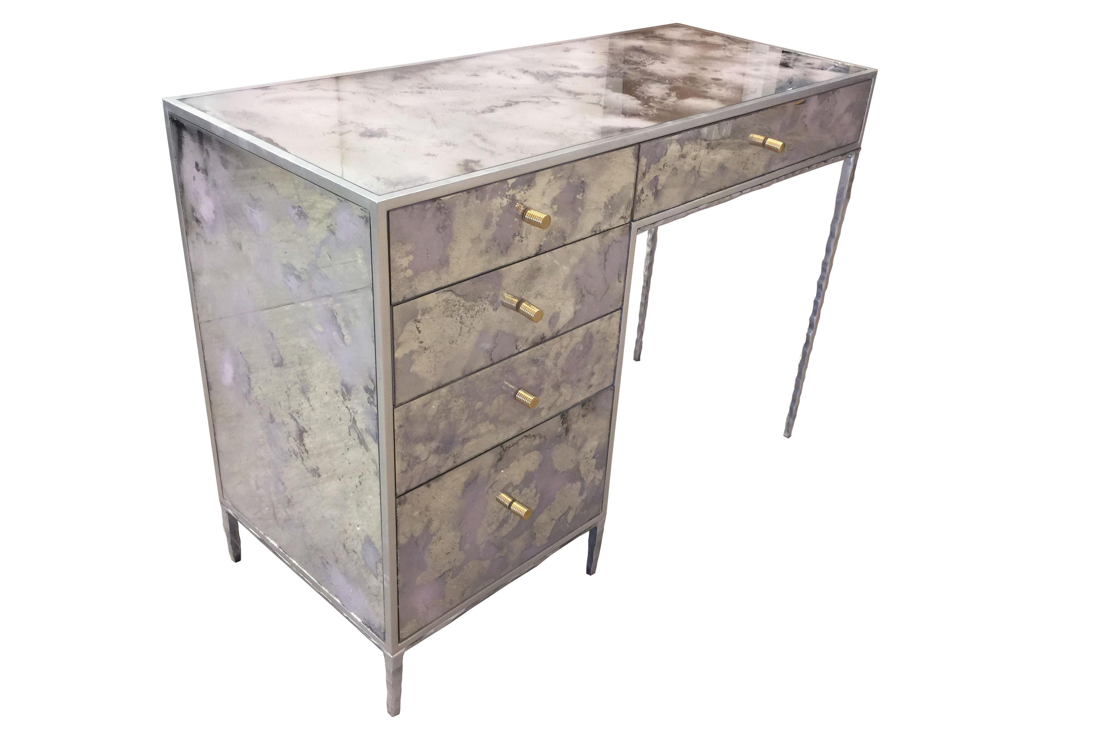 The églomisé pink dust vanity by Ercole Home has a 5-drawer, with silver leaf wood finish. Hand painted églomisé glass panels are inset on the surface.
There are five metal pulls in brass finish.
The hand-hammered metal base is in silver