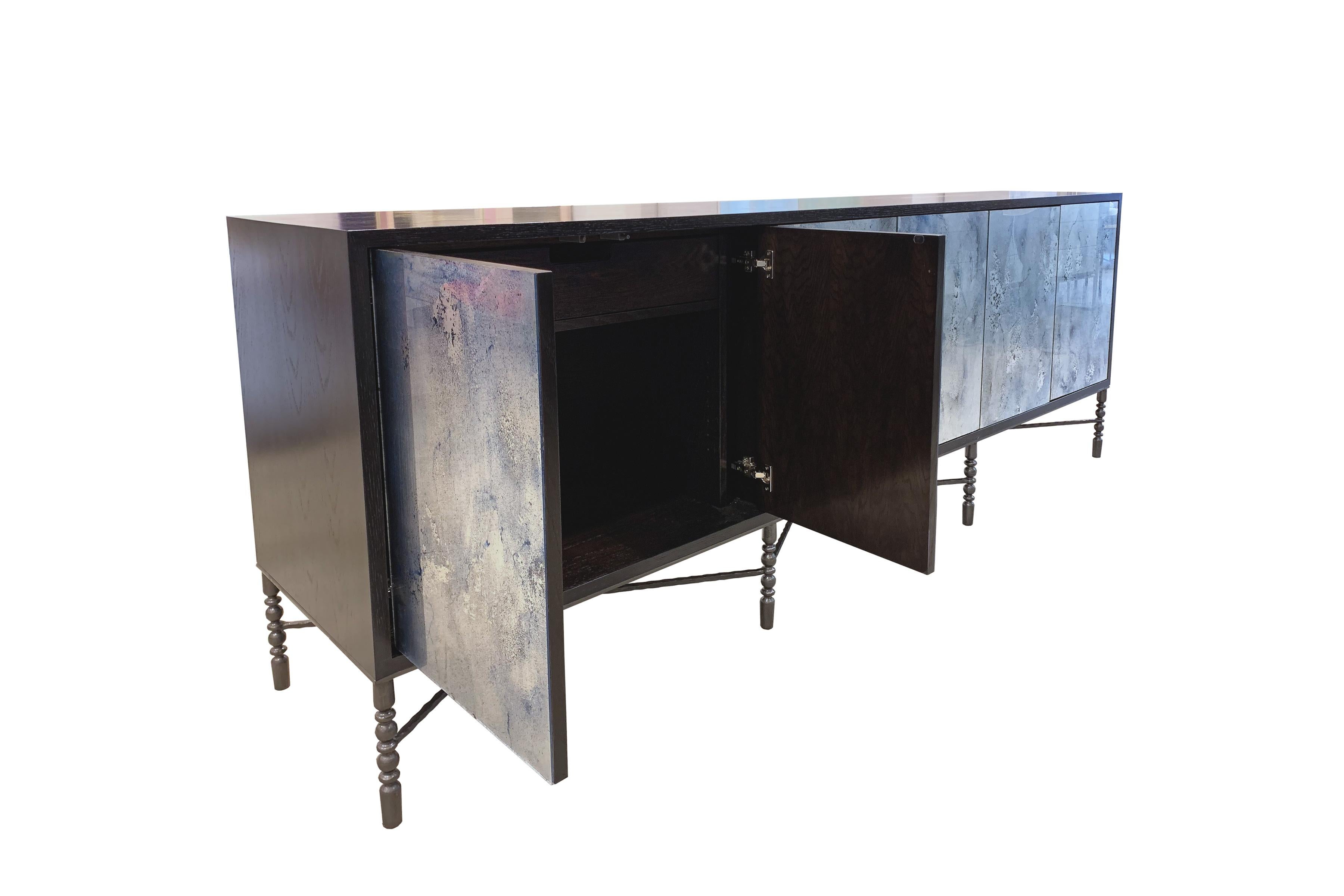 The Mystic buffet or credenza by Ercole home has a 6-door front, with Espresso wood finish on oak.
Hand-painted glass panels in Midnight Moon are on the door surface.
The decorative vintage style base with hand-hammered X-shape stretchers in