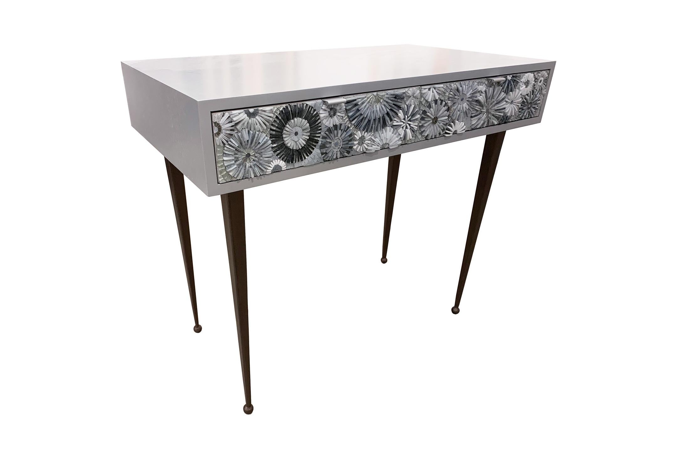 La scrivania/vanity Pavia Blossom di Ercole Home ha 2 cassetti e una finitura in legno grigio cielo su rovere.
Mosaici di vetro tagliato a mano in verde-blu e turchese decorano i frontali dei cassetti con motivi a fiore (fiori