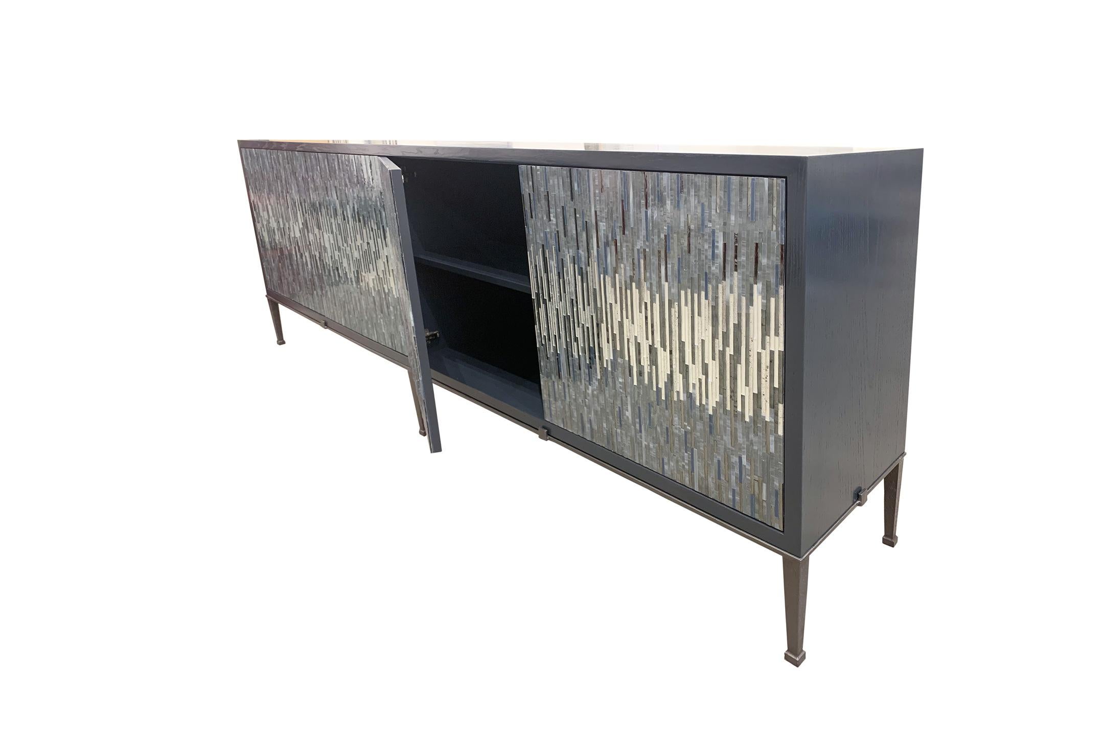 The industrial buffet by Ercole Home has a 4-door front, with dark gray lacquer wood finish on oak. Handcut glass mosaics in gray, silver, Pewter decorate the surface in a continuous wave pattern.
The metal Milano base with small decorative tabs is