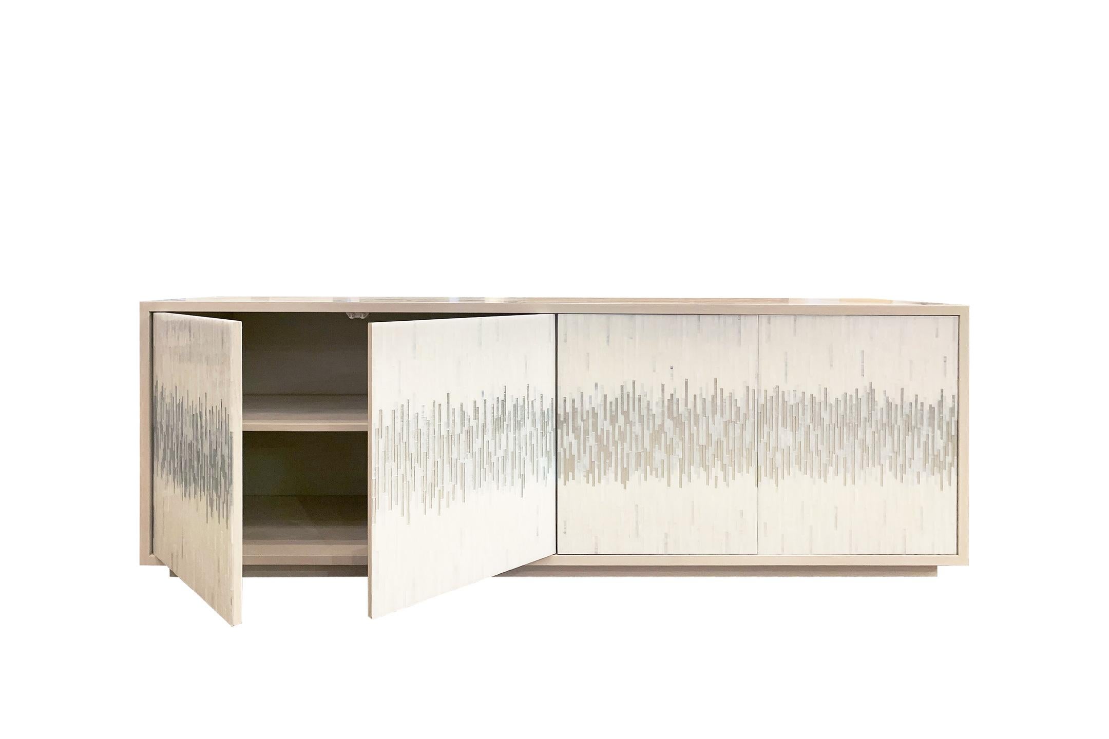 The platform wave buffet by Ercole Home has a 4-door front, with washed ivory wood finish on oak. Handcut glass mosaics in icy white and silver, wispy white silver decorate the surface in a continuous wave pattern.
There is one adjustable interior