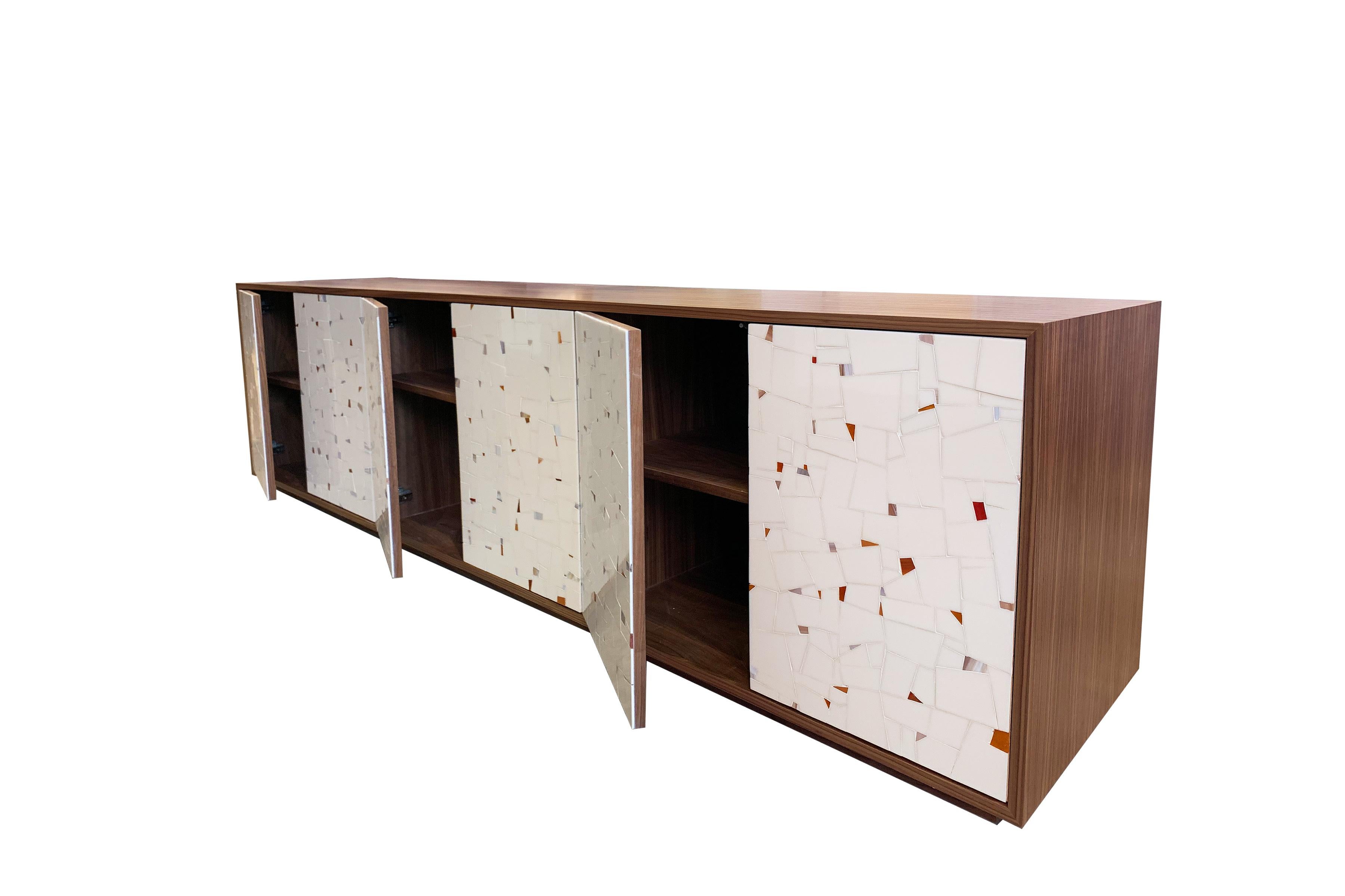 The platform buffet by Ercole Home has a 6-door front, with a natural wood finish on Walnut. Handcut glass mosaics in Light ivory/pink glass mosaic decorate the surface in a continuous Terrazzo pattern. 
There is one adjustable interior shelf in