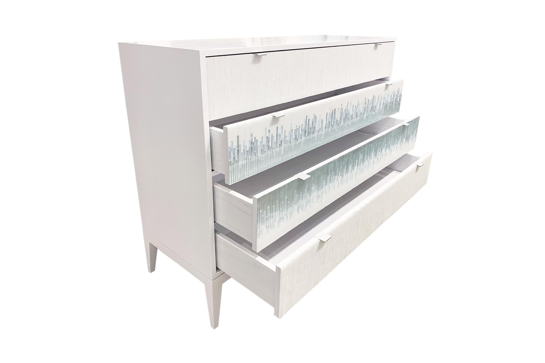 The Milano chest of drawers by Ercole Home has a 4-drawer front, with painted white wood finish on oak. Hand cut glass mosaics in icy white, wispy white silver, and silver decorate the surface in a continuous wave pattern.
There are two metal edge