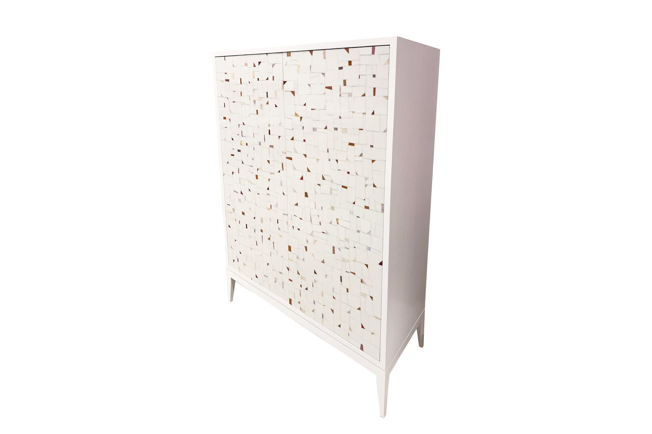 The Milano bar cabinet by Ercole Home has a 2-door front, with a Painted White wood finish on oak. Handcut glass mosaics in Light ivory/white glass mosaic decorate the surface in a continuous Terrazzo pattern.
Custom sizes and finishes are