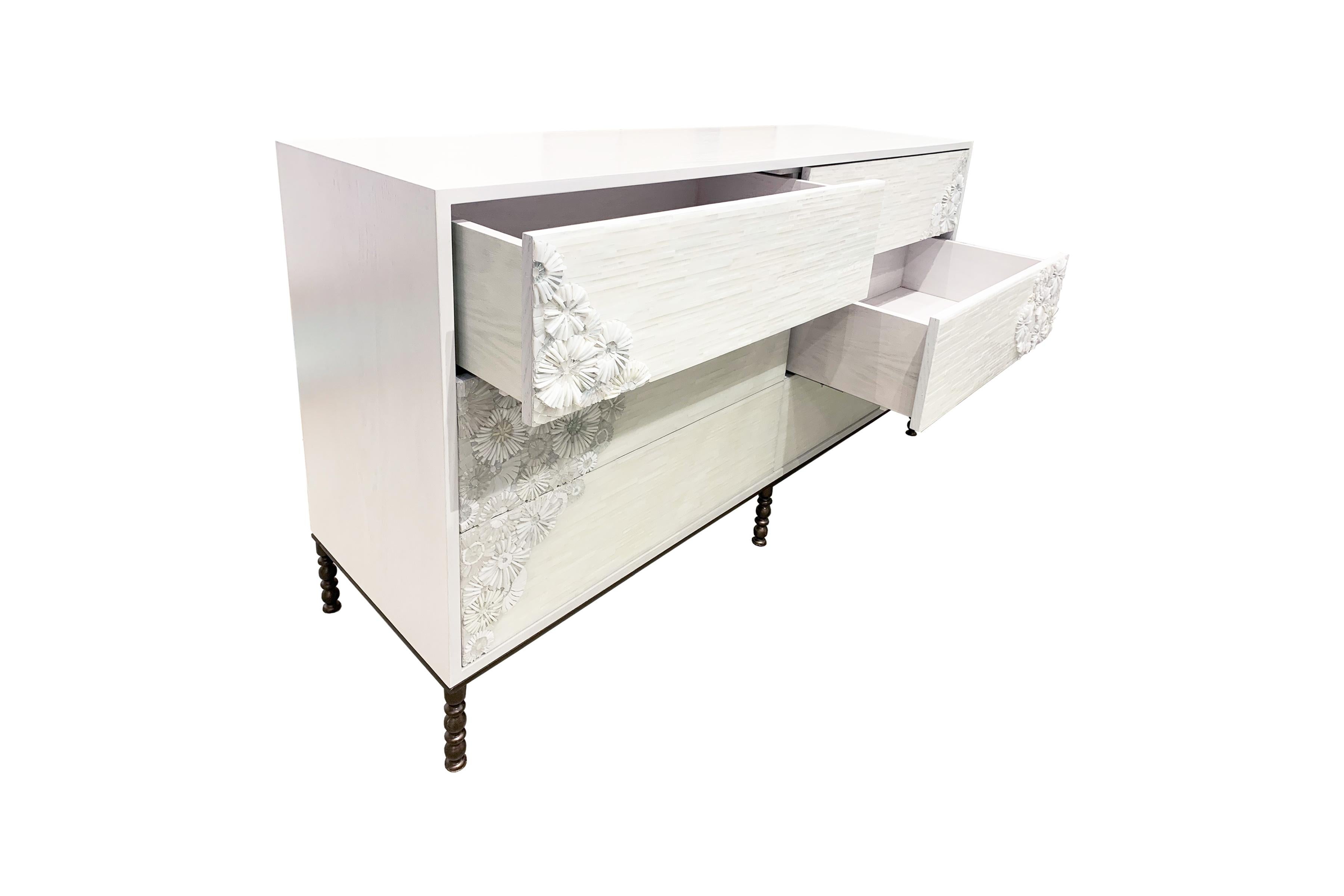 The Blossom chest of 6 drawers by Ercole Home has a 6-drawer front, with white wash finish on oak wood.
Handcut glass mosaic in variety shades of white and ivory decorate the surface in Blossom and stipe mosaic pattern.
The decorative metal base