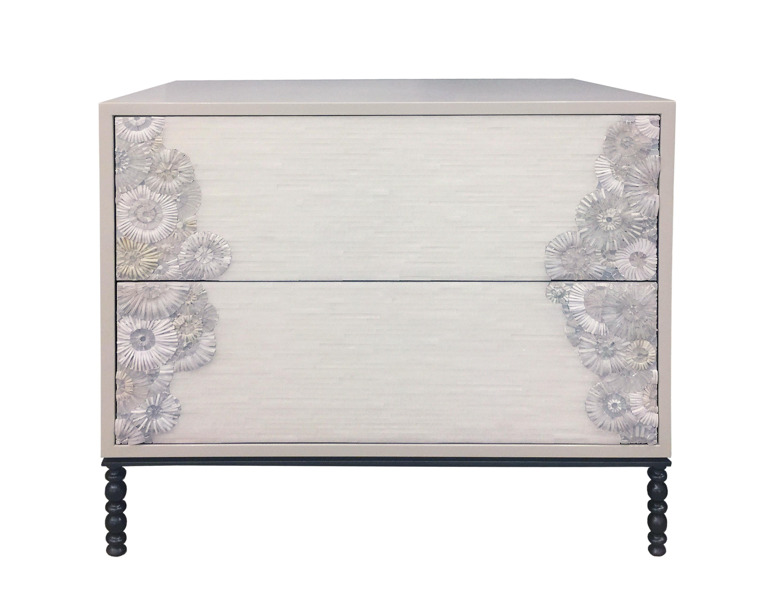 The Blossom nightstand by Ercole Home has a 2-drawer front, with Misty Gray lacquer wood finish.
Handcut glass mosaic in variety shades of white and ivory decorate the surface in Blossom and stipe mosaic pattern.
The decorative metal base is in Dark