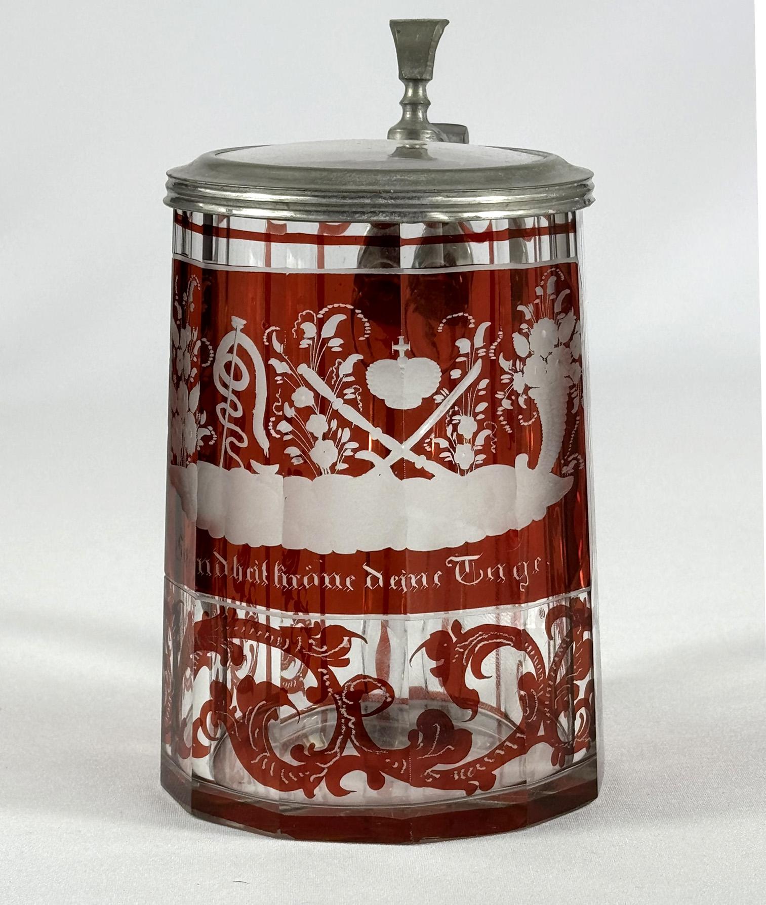 Une belle chope en verre et en verre taillé, décorée de lazure rouge et de symboles gravés. Le couvercle est une combinaison de verre et d'étain. La veduta est gravée du symbolisme d'un serpent représentant la santé, d'une corne d'abondance