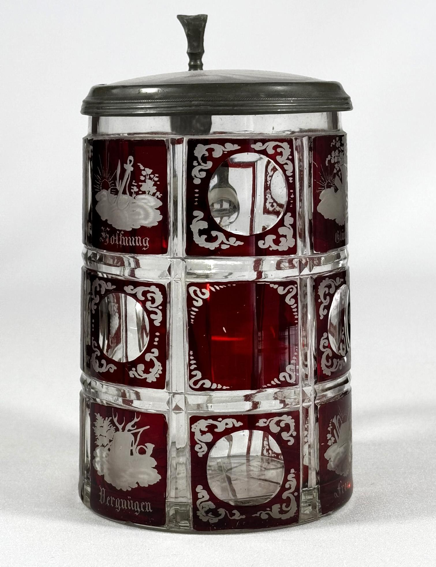 Une belle chope en verre et en verre taillé, décorée de lazure rouge et de symboles gravés. Le couvercle est une combinaison de verre et d'étain. Le verre est divisé par des entailles en 15 petites veduta, chacune avec des gravures de symboles. Les