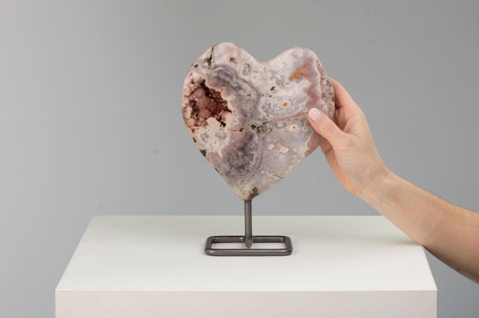 An attractive geode section cut and polished into a heart shape, revealing
white quartz layers with various agate layers. A cavity to the left with pink
druze resembling cotton candy.

This piece was legally and ethically sourced directly in the
