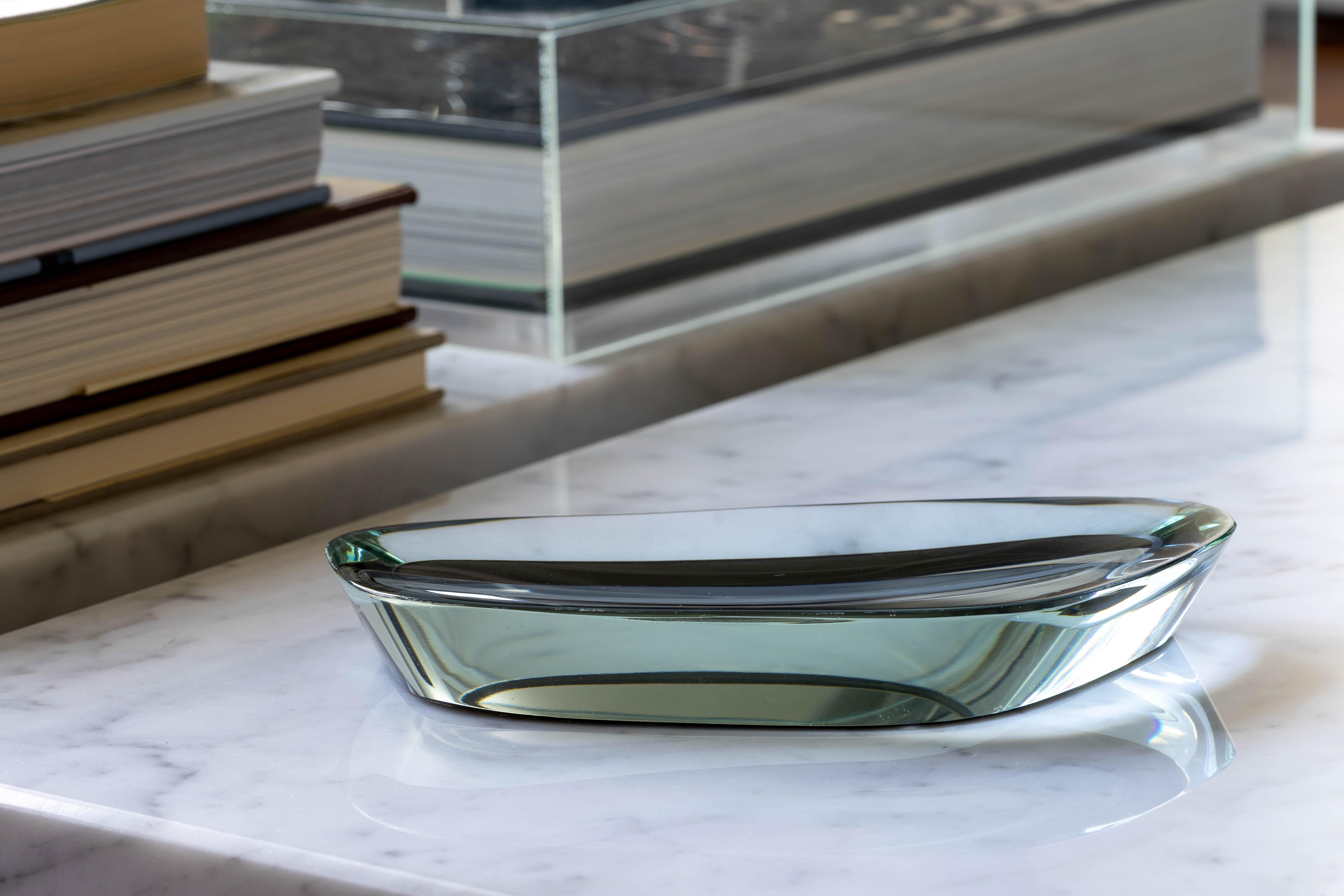 A curved, cut, and polished blue-green glass dish with a silver-mirrored bottom. Produced by Fontana Arte in the late 1950s, the abstract form of the dish is coupled with a slightly concave surface and mirrored base that creates a constantly