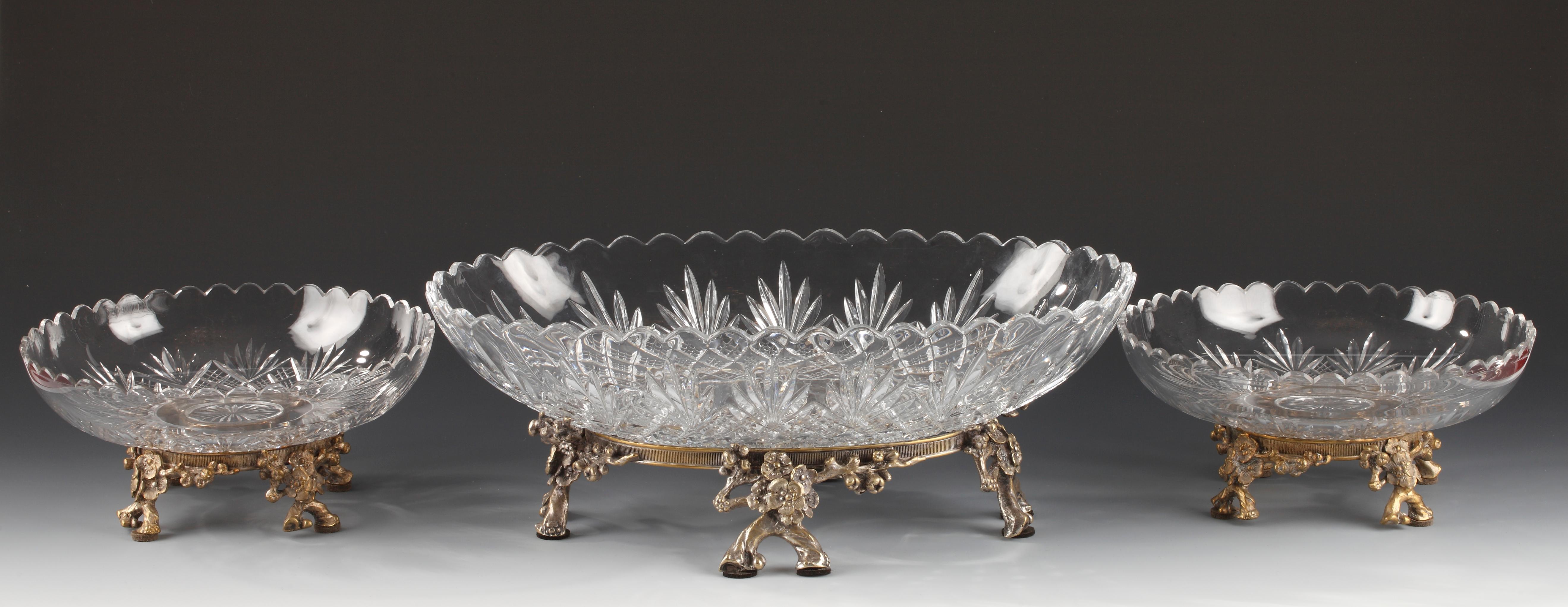 Elegant centerpiece attributed to Baccarat, composed of an oval cut-crystal cup and two circular cut-crystal cups decorated with stylized palmettes on a grid background, resting on a silvered bronze mount representing blooming branches.

Oval cup: