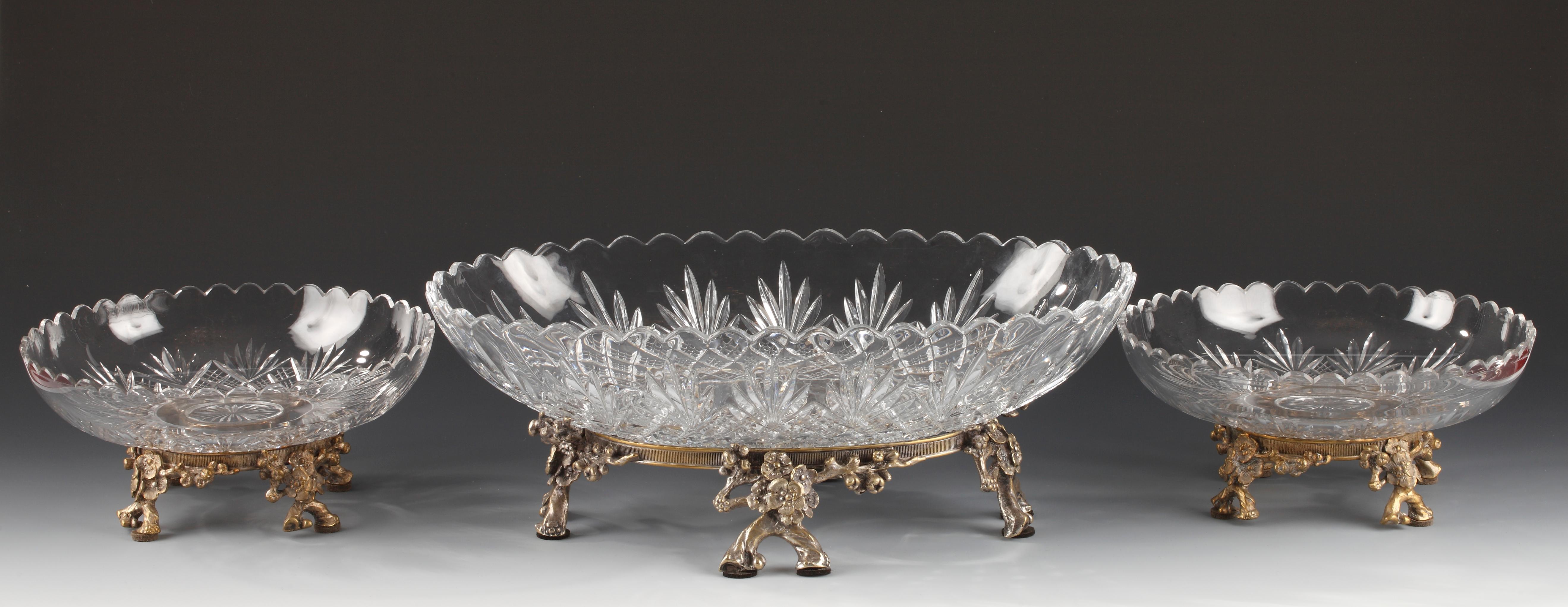 Elegante centro de mesa atribuido a Baccarat, compuesto por una copa ovalada de cristal tallado y dos copas circulares de cristal tallado decoradas con estilizadas palmetas sobre fondo cuadriculado, que descansan sobre una montura de bronce plateado