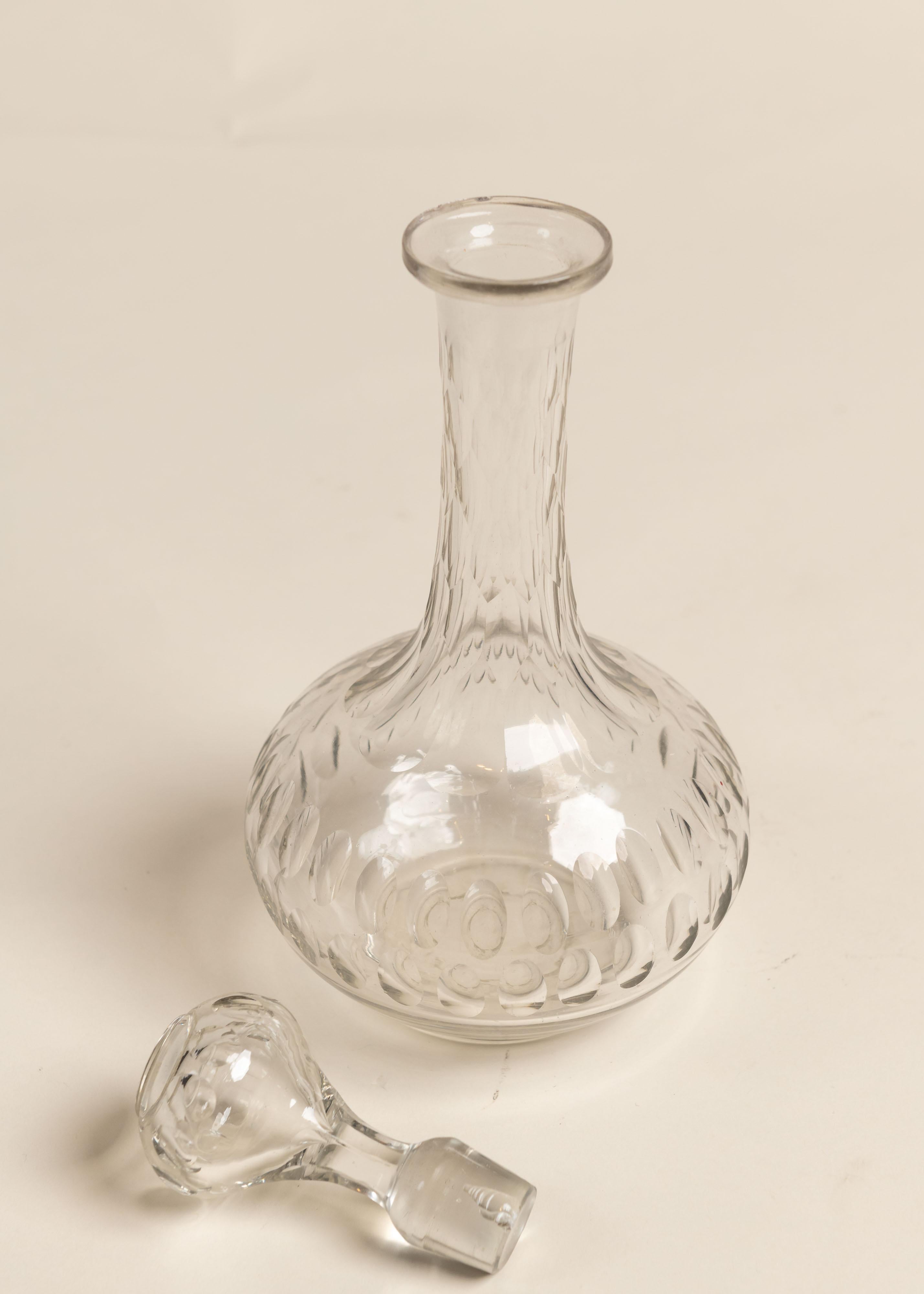 An elegant cut crystal decanter featuring a bulbous base that tapers upwards into a tall, slender neck, topped with a distinct stopper. Faceted design enhances the look and feel of this piece. Great on its own, perfect in a grouping.