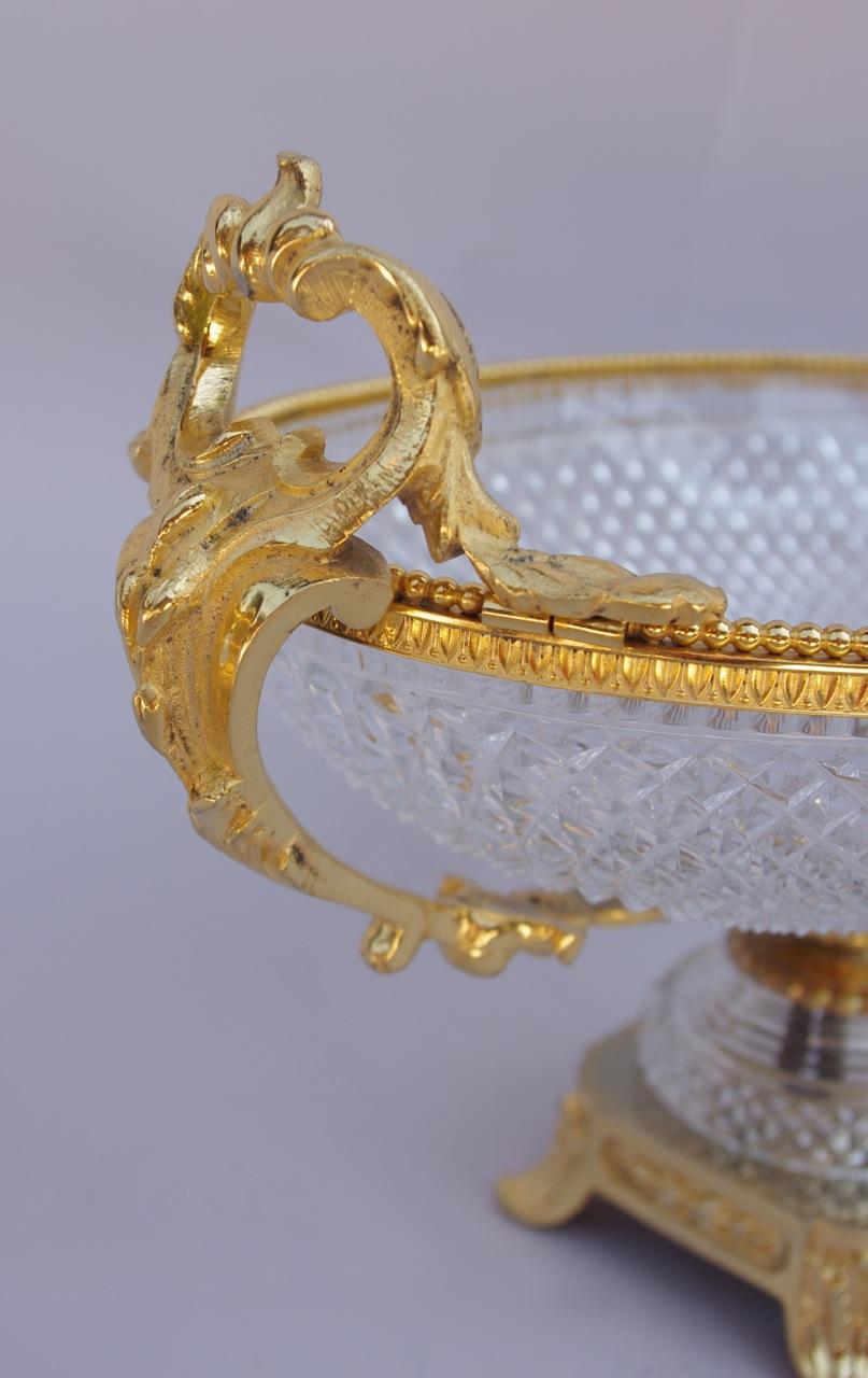 Ovaler Becher aus Sèvres-Kristall mit Diamantschliff und vergoldeter Bronzefassung auf quadratischem Sockel mit vier Beinen. Der Kragen des Bechers ist mit Wasserblättern und Perlenfriesen verziert, wo die vegetabilen, stilisierten Henkel im