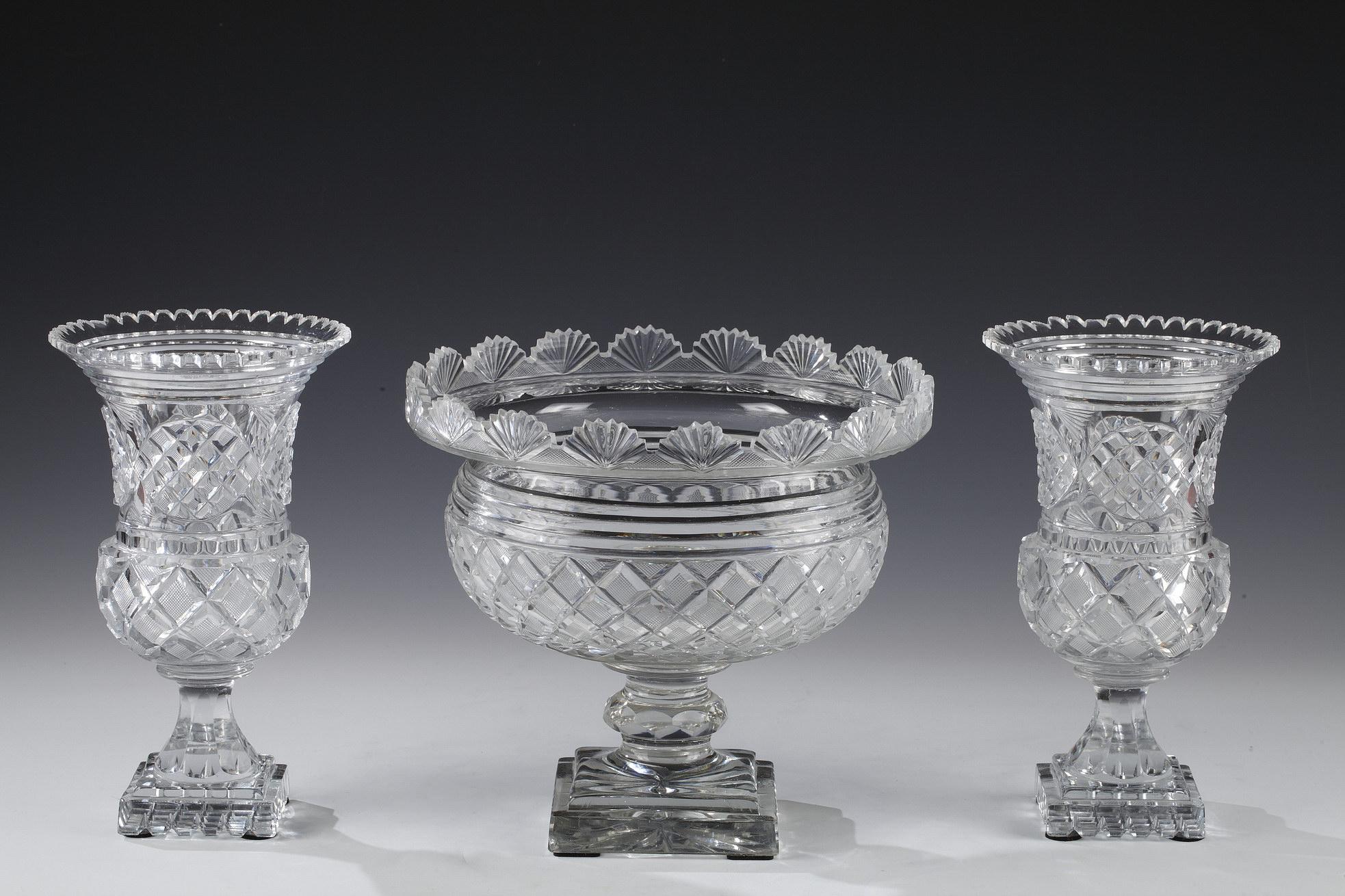Elegant cut crystal set, composed of a circular goblet on pedestal and two Medici vases.
The whole is engraved with braces, and serrated edges on the flared neck. They rest on a square base.

Measures: Center height 25 cm (9.8 in.), diameter 27 cm