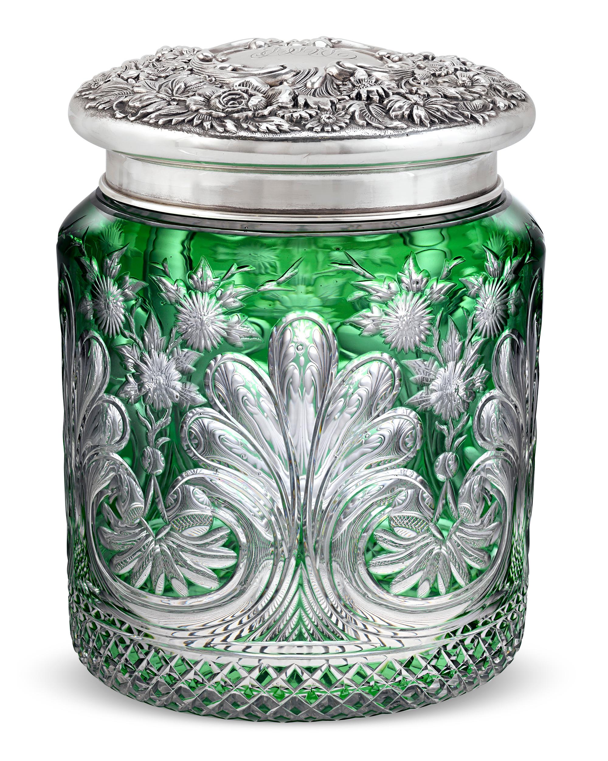 Vivid color and precise cutting distinguish this glass humidor by celebrated English glassmakers Stevens & Williams. Floral intaglio decoration and a masterfully cut scroll motif are formed from deep emerald green glass cut to clear. The vessel is