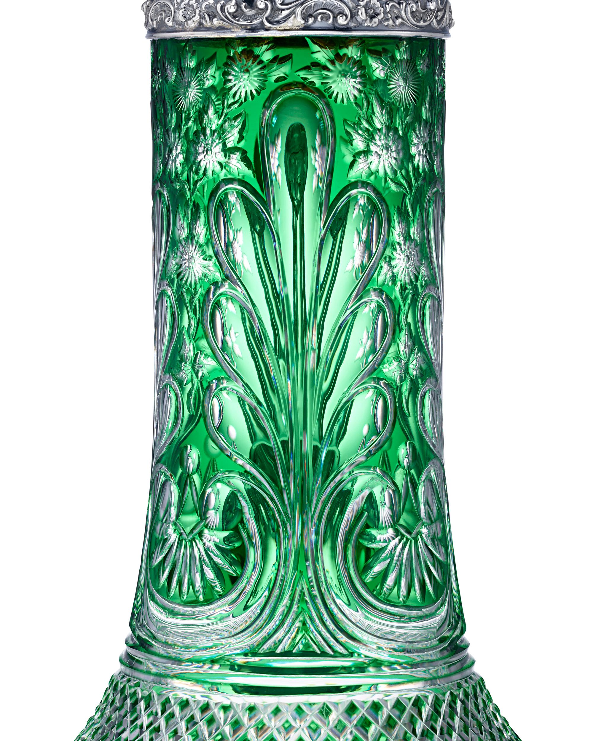 This mesmerizing green glass pitcher is set apart by its gorgeous color, enchanting design, and exquisitely repousséd silver top. Masterfully crafted by celebrated English glassmakers Stevens & Williams, the elaborate decoration is brilliantly cut