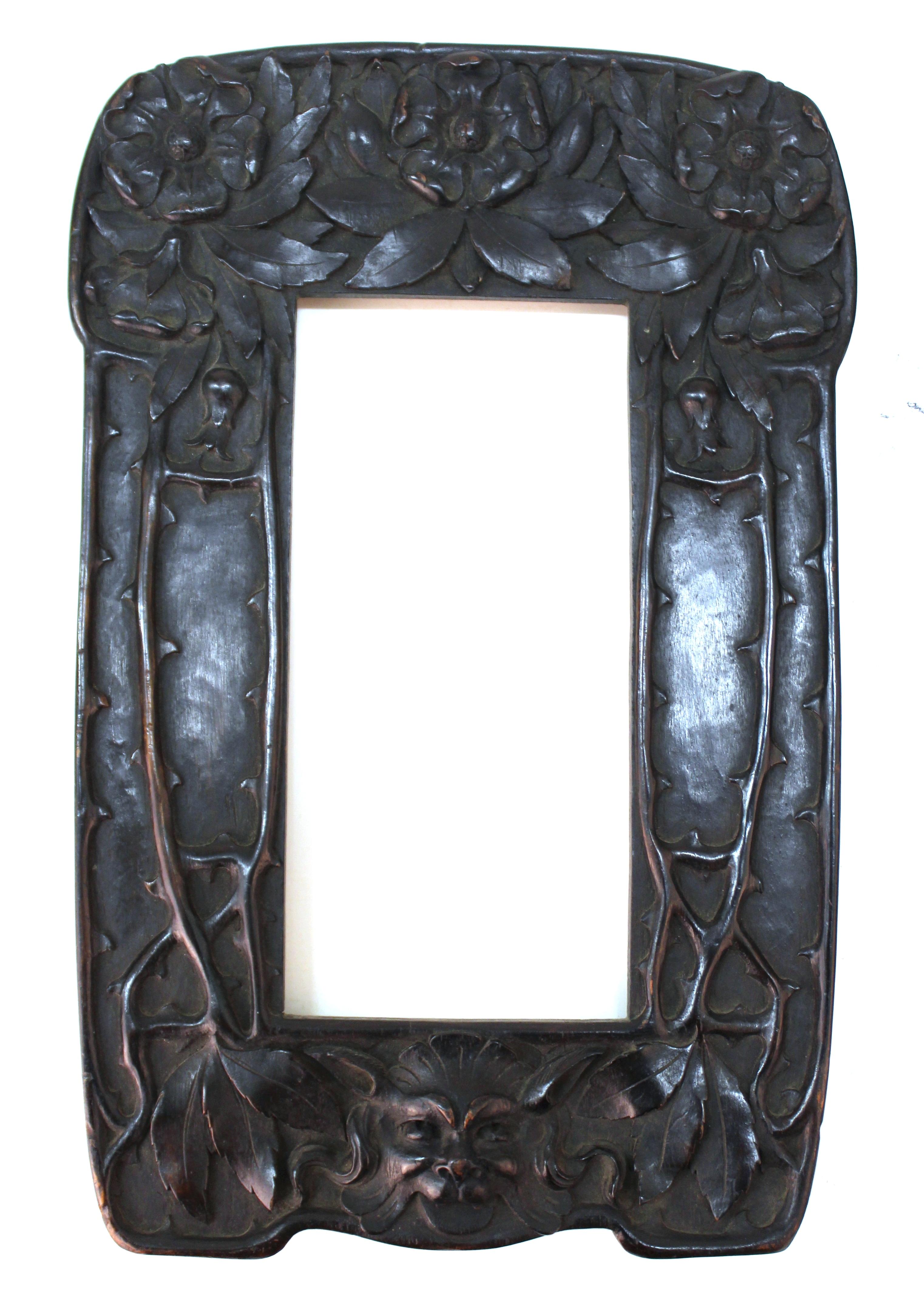 Italian Art Nouveau mirror with an elaborately carved wood frame, created by Cutler & Girard in Italy. The frame has carved roses on the upper part, thorns on the sides and the head of a grotesque on the bottom part. The piece has a makers label on