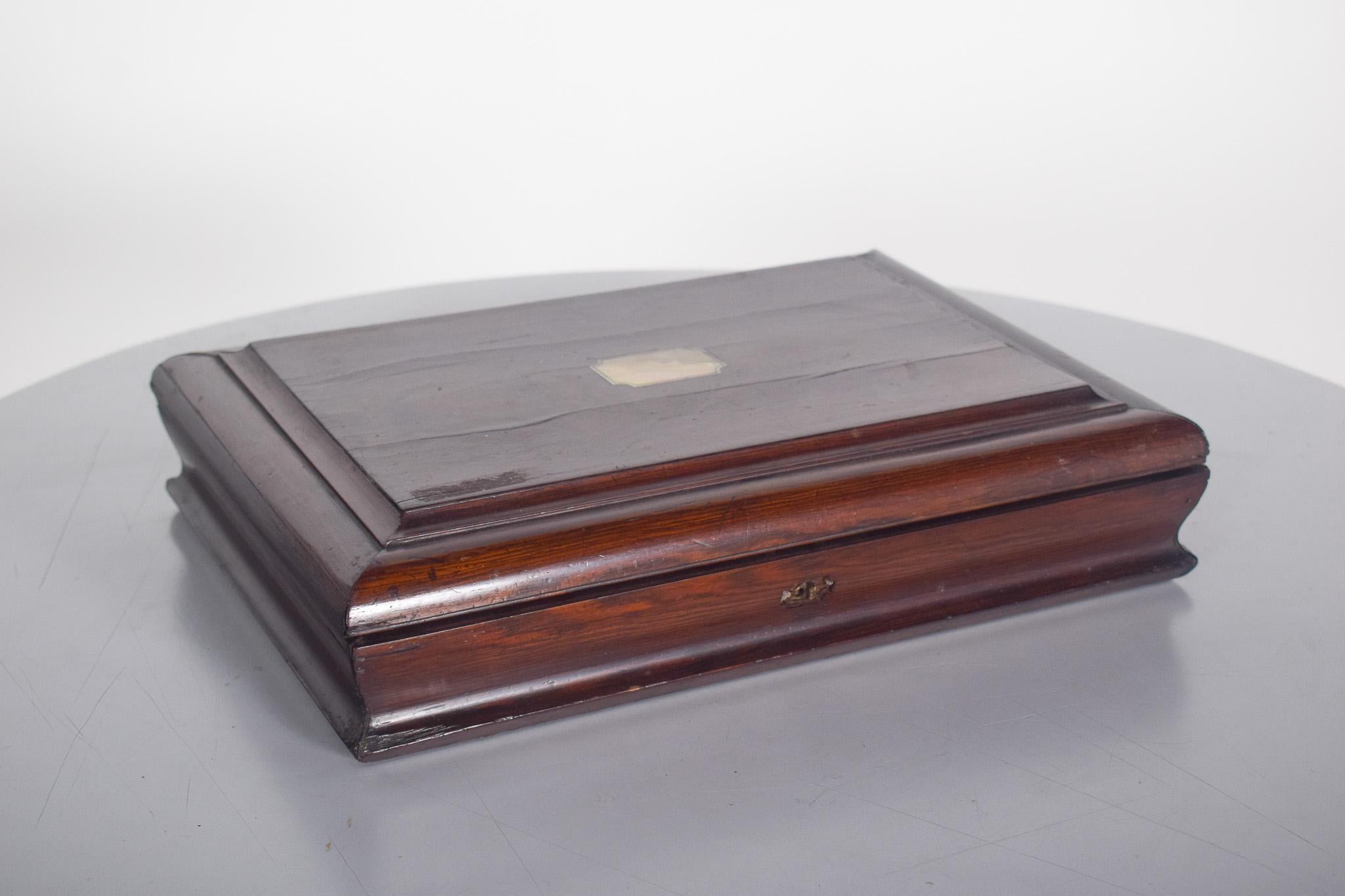 Coffret à couverts, en bois de rose. Avec un design classique et une finition vernie.
Le couvercle comporte une plaque métallique décorative au centre. La structure du boîtier présente des cadres sculptés en douceur, soulignant son esthétique