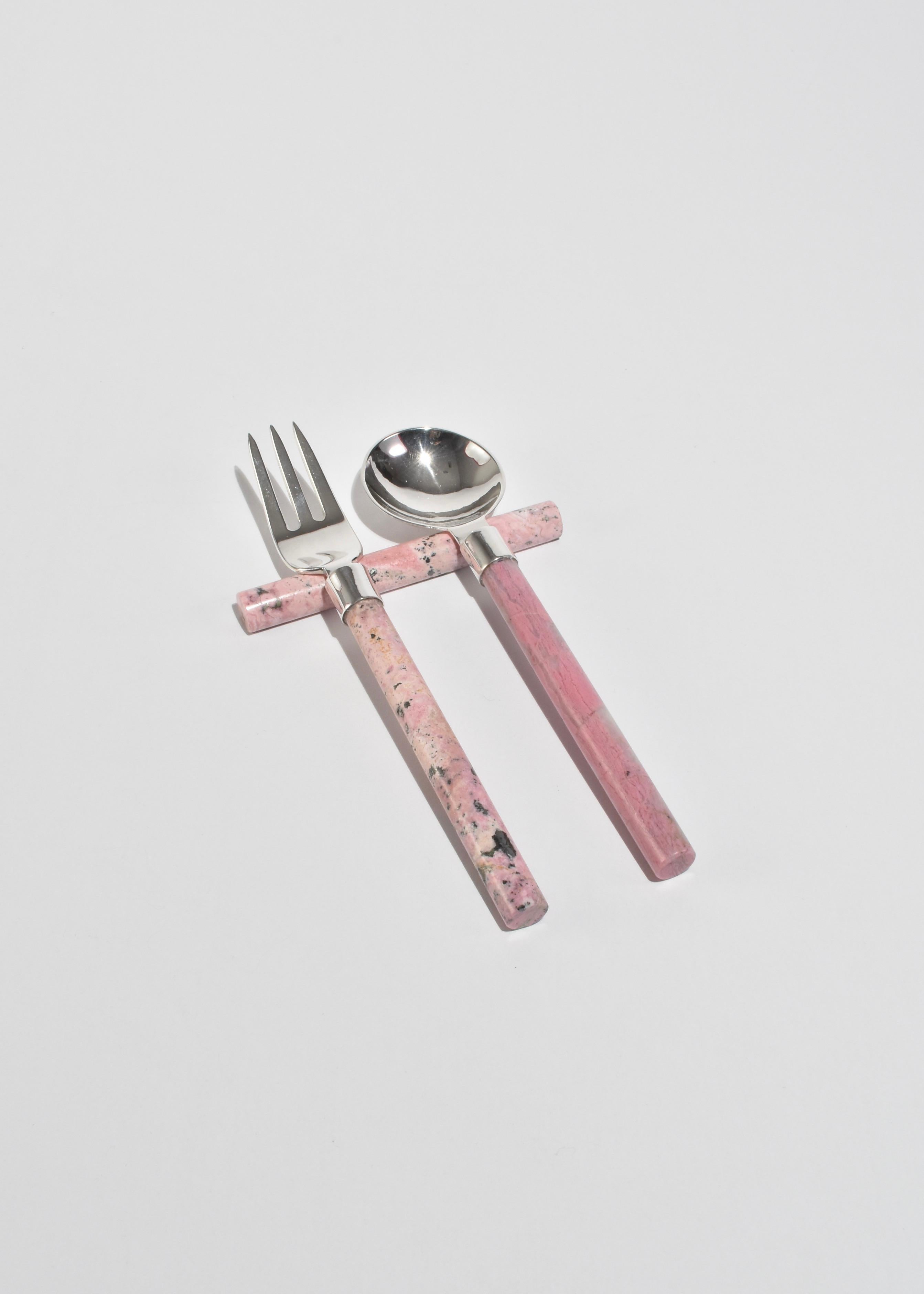 A sculptural cutlery set, combining silver-plated brass with pink rhodonite stone handles for a tactile, refined dining experience. Each set includes five pieces: a dinner fork, salad fork, dinner knife, soup spoon, and dessert spoon. Each piece is